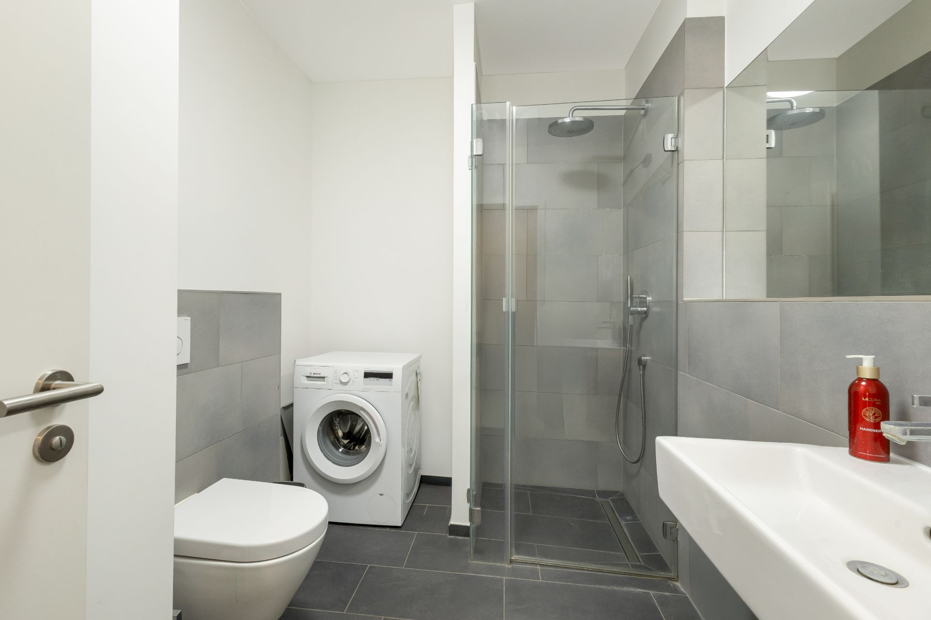 Modernes Badezimmer mit Waschmaschine, Dusche, WC und Waschbecken.