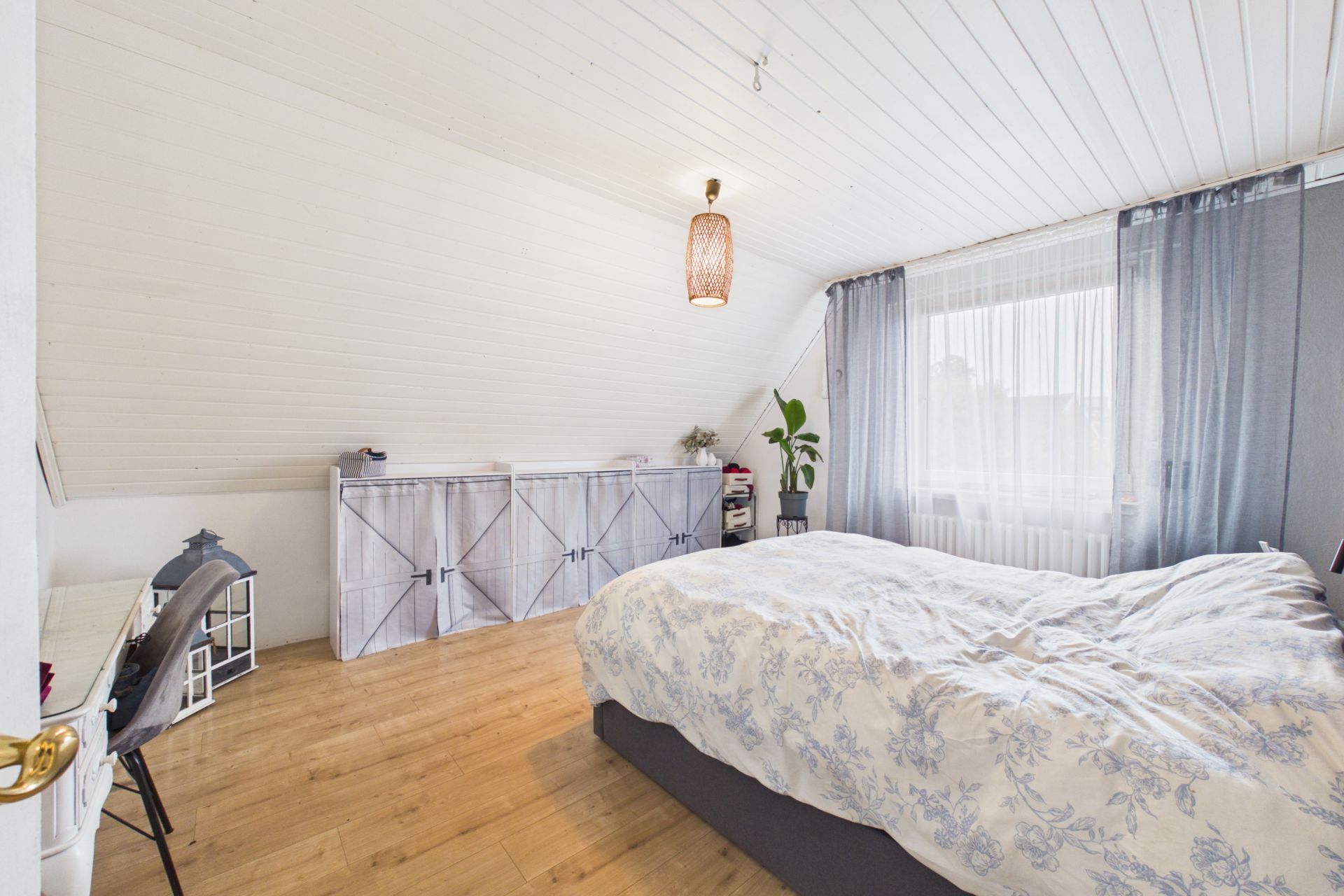 Helles Schlafzimmer mit großem Bett, Holzfußboden, Schränken und einem Fenster mit Vorhängen.