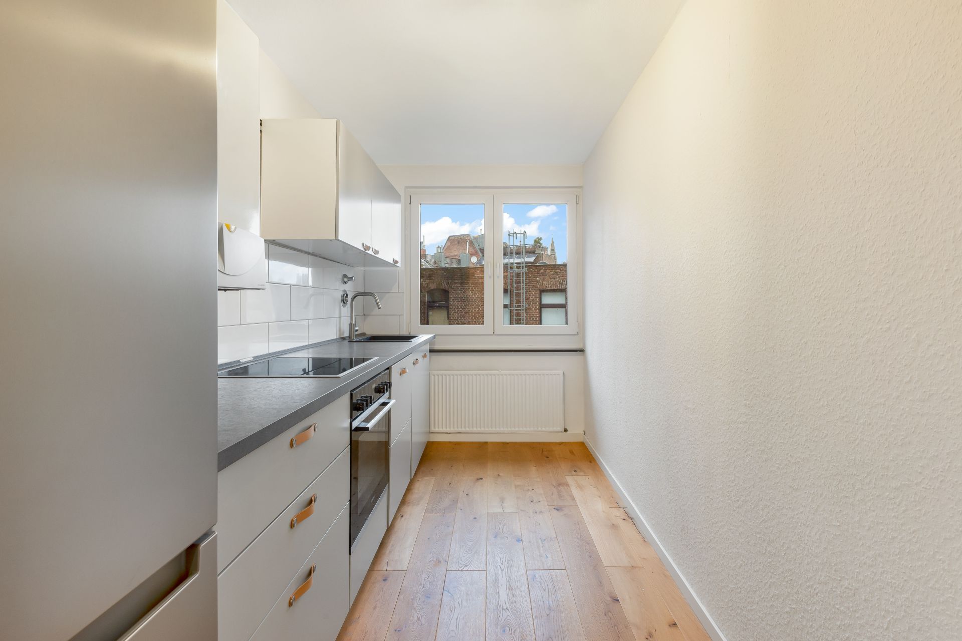 Schmale Küche mit weißen Schränken, Herd, Spüle und Fenster, Holzboden.