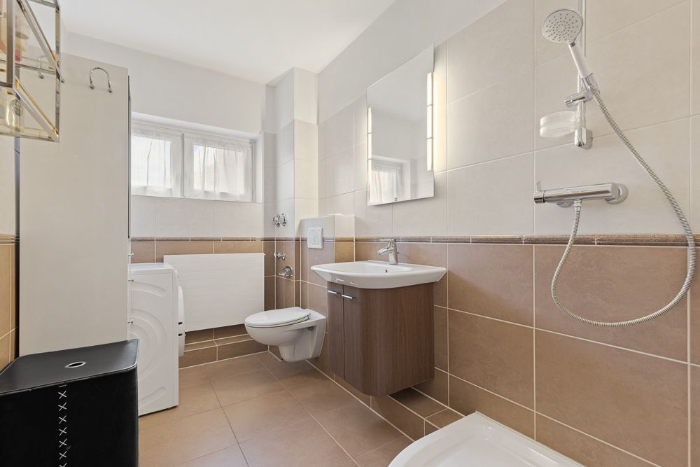 Modernes Badezimmer mit Dusche, Waschbecken, Spiegel, WC und Waschmaschine.