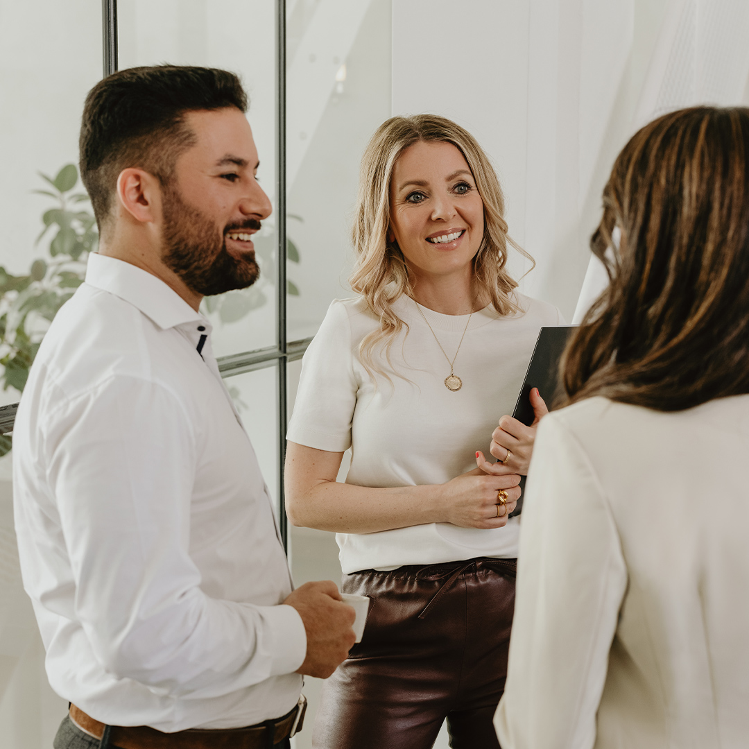 Drei Menschen stehen in einem hellen Raum und unterhalten sich freundlich.