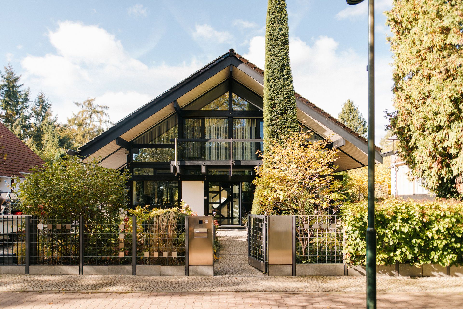 Modernes Einfamilienhaus mit Glasfront, Garten und Zaun, von Bäumen umgeben.