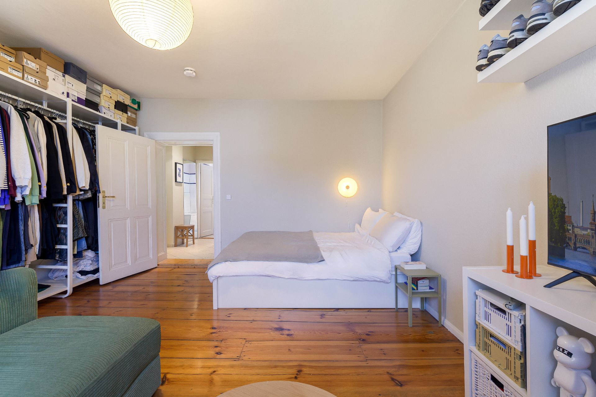 Modernes Schlafzimmer mit offenem Kleiderschrank, Doppelbett und Fernseher auf Holzfußboden.