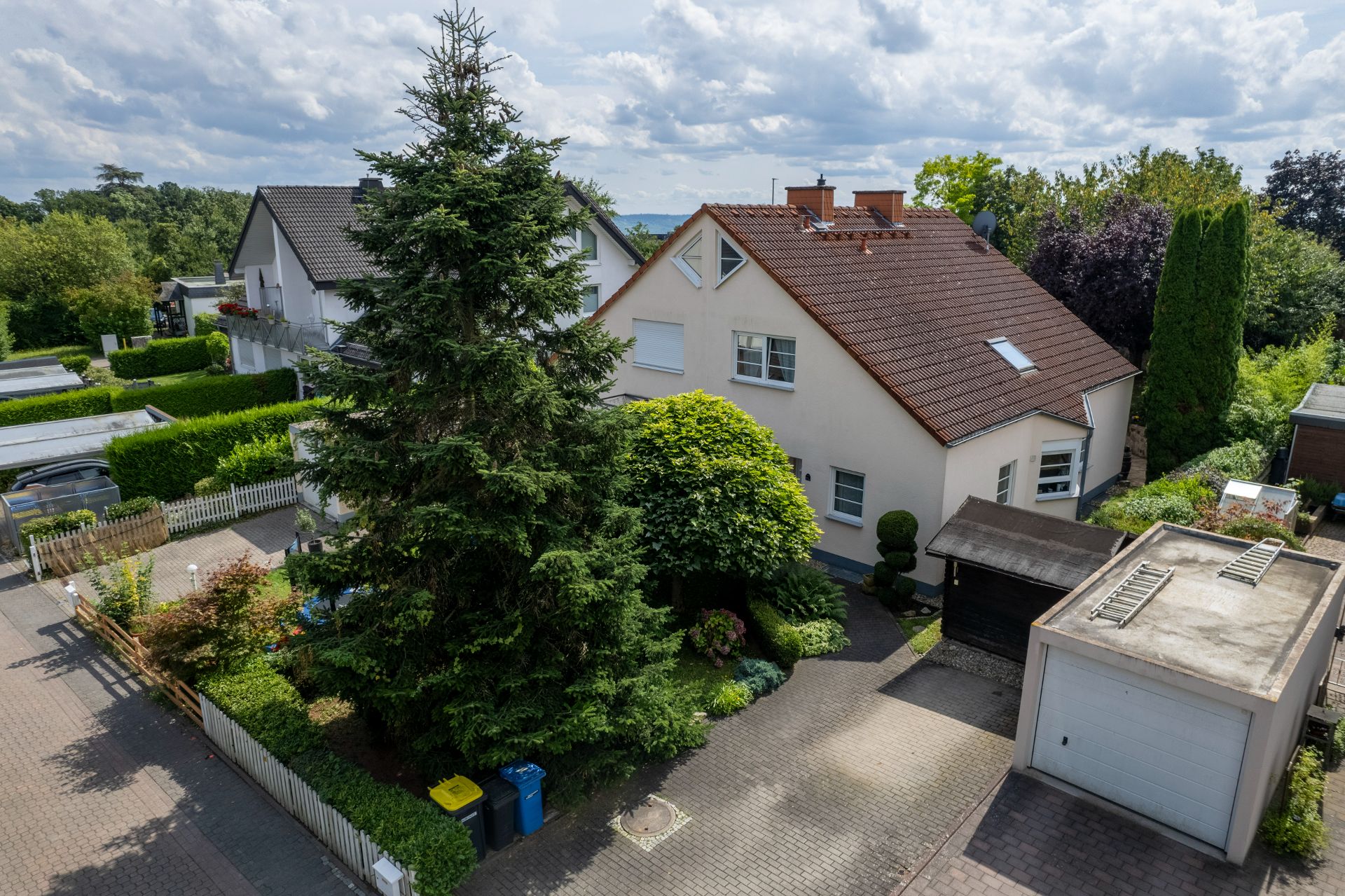 Einfamilienhaus mit Garten, Garage und großen Bäumen in einer Wohnsiedlung.