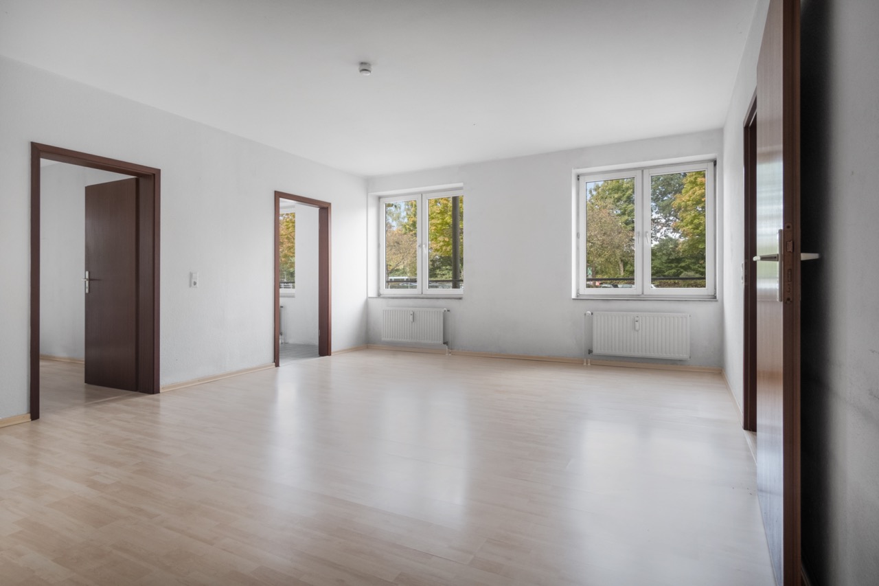 Heller, leerer Raum mit zwei Fenstern, Laminatboden und weißen Wänden.