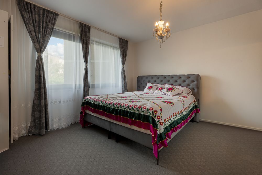 Schlafzimmer mit Doppelbett, Blumenbettwäsche, grauen Vorhängen und Kronleuchter.