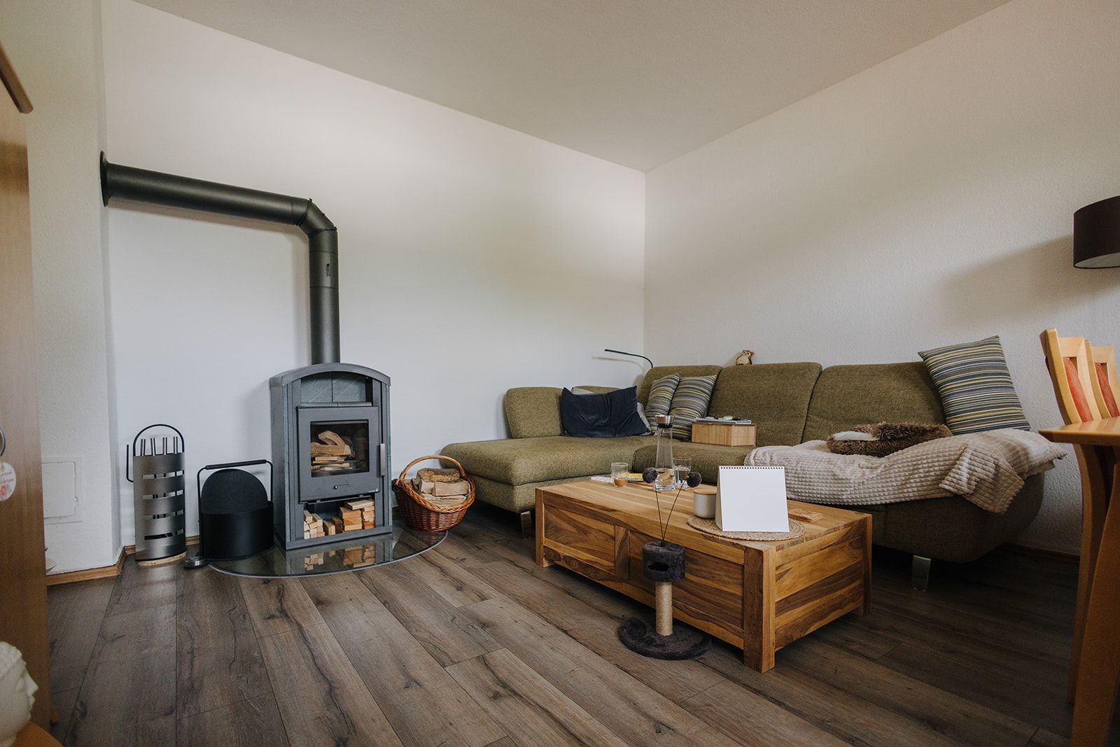 Wohnzimmer mit grünem Sofa, Holzofen und Couchtisch auf Holzboden.