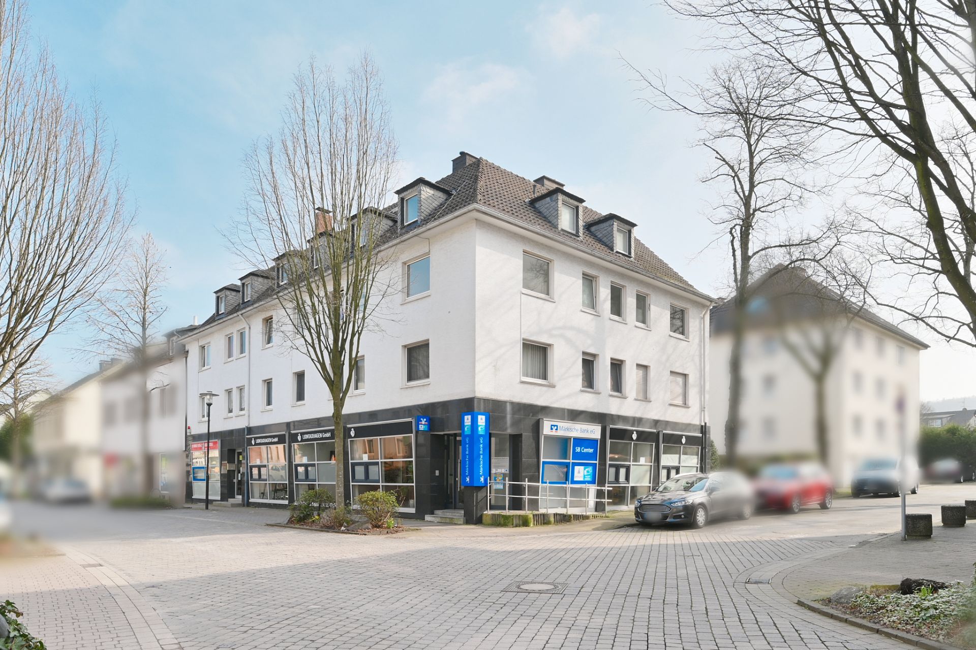 Eckhaus mit weißer Fassade, mehreren Fenstern und Ladengeschäften im Erdgeschoss.