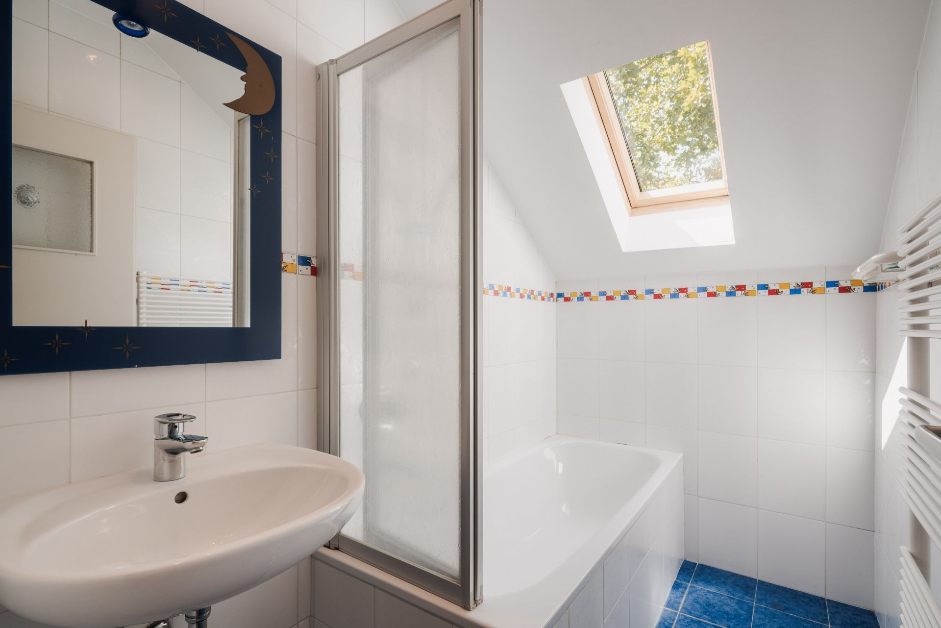 Helles Bad mit Badewanne, Waschbecken, Spiegel und Dachfenster.
