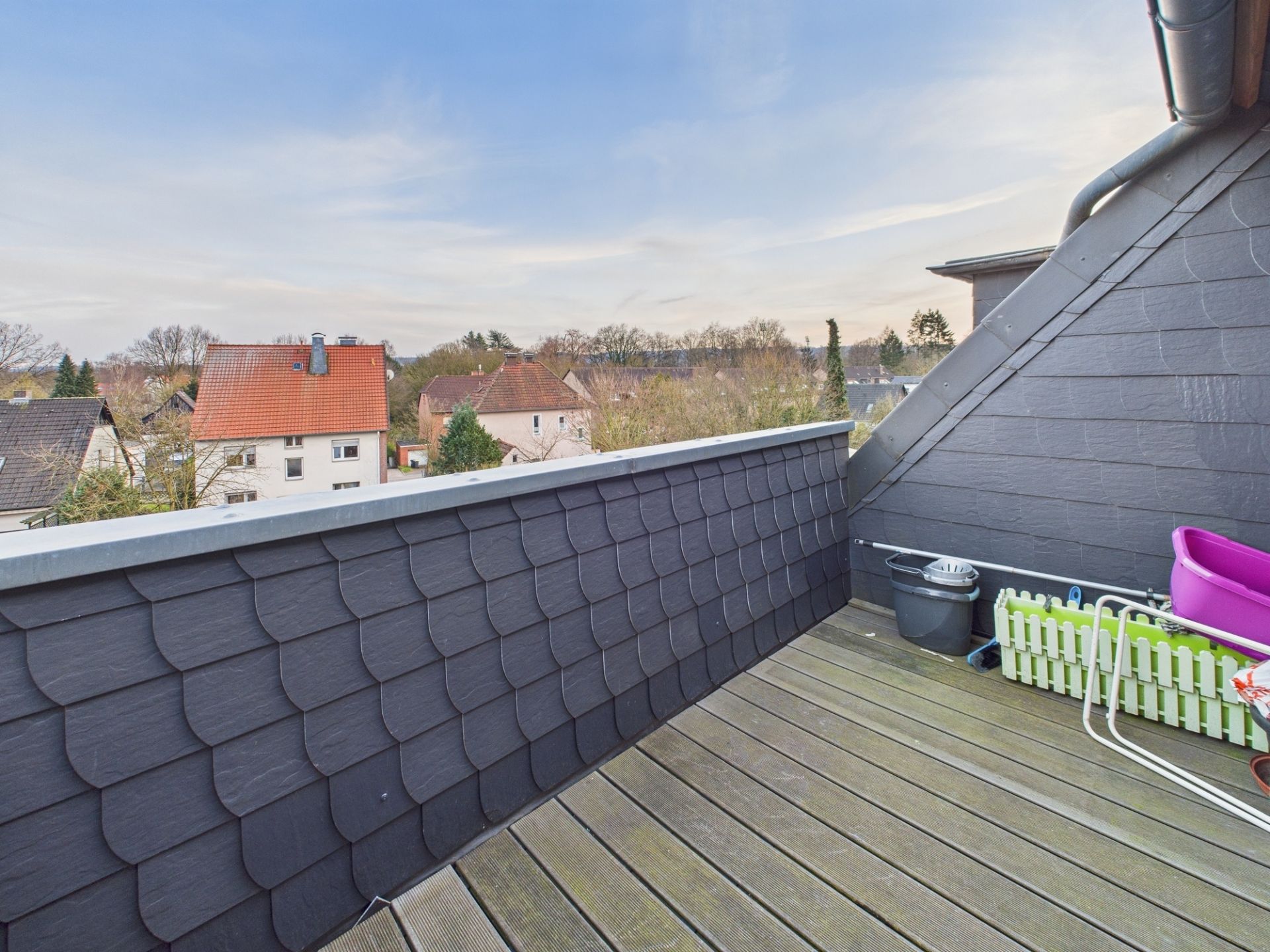 Dachterrasse mit Holzfußboden und Blick auf Nachbarhäuser und Bäume.