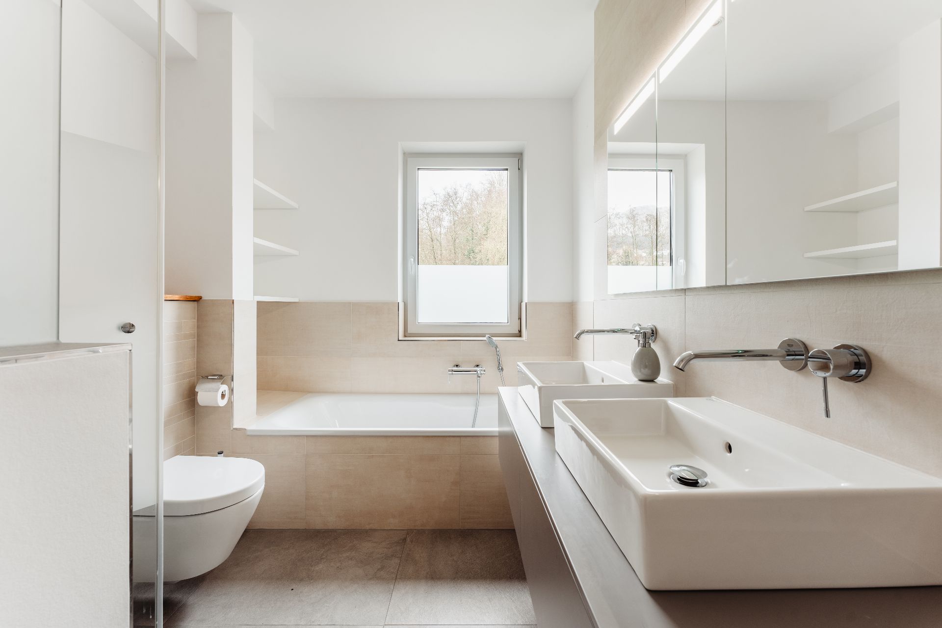 Modernes Badezimmer mit Badewanne, zwei Waschbecken, Toilette und großem Fenster.