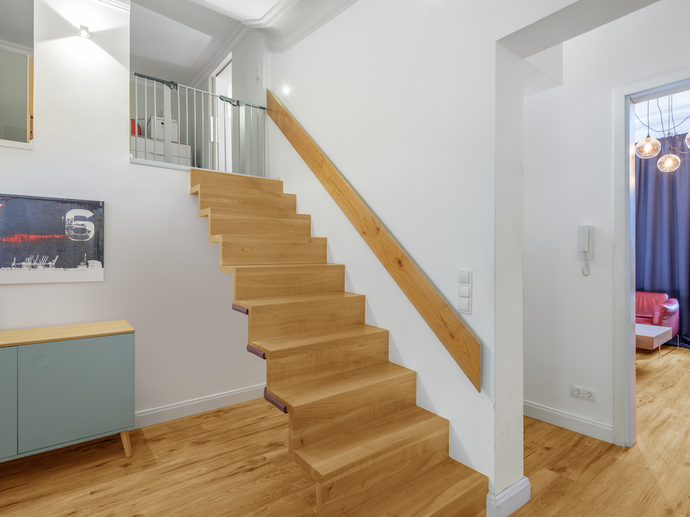 Moderne Holztreppe in einem hellen Flur mit Holzboden und Gemälde an der Wand.