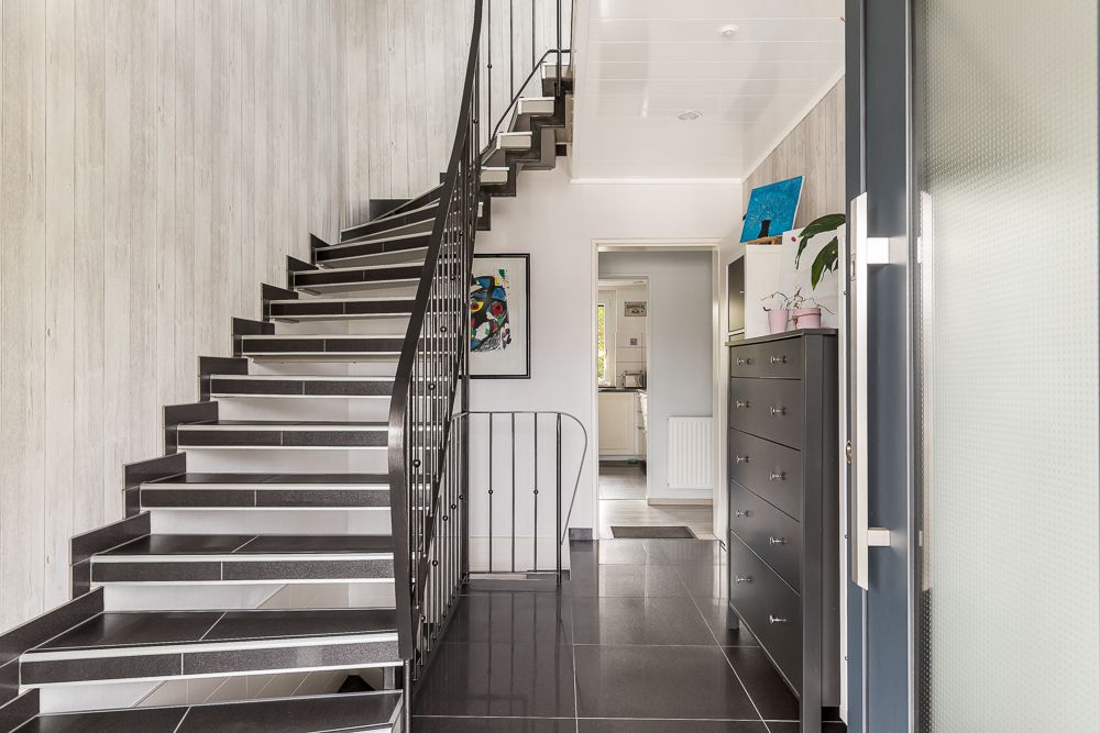 Heller Flur mit schwarzer Treppe, Kommode und Fliesenboden, Blick in die Küche.