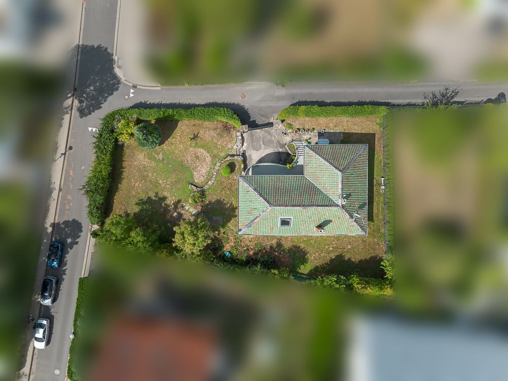 Luftaufnahme eines Einfamilienhauses mit Garten und Auffahrt auf einem umzäunten Grundstück.