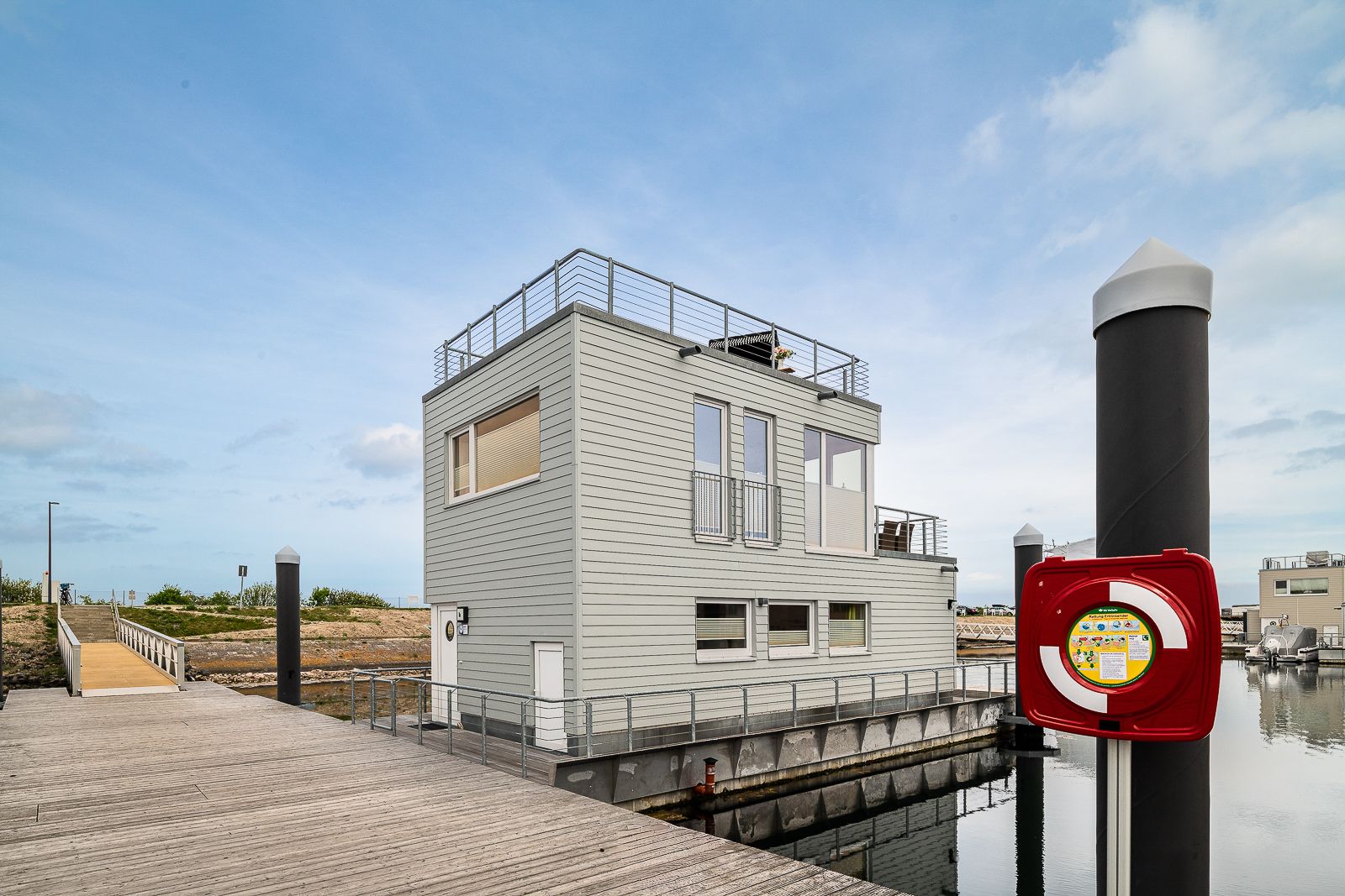 Modernes Hausboot mit zwei Etagen, großer Dachterrasse und Geländer am Steg.