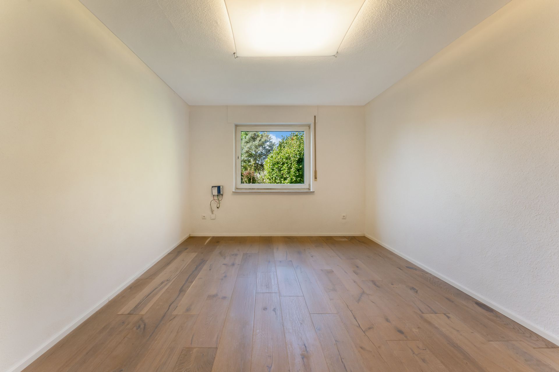 Leerer Raum mit Holzfußboden, einem Fenster und cremefarbenen Wänden.