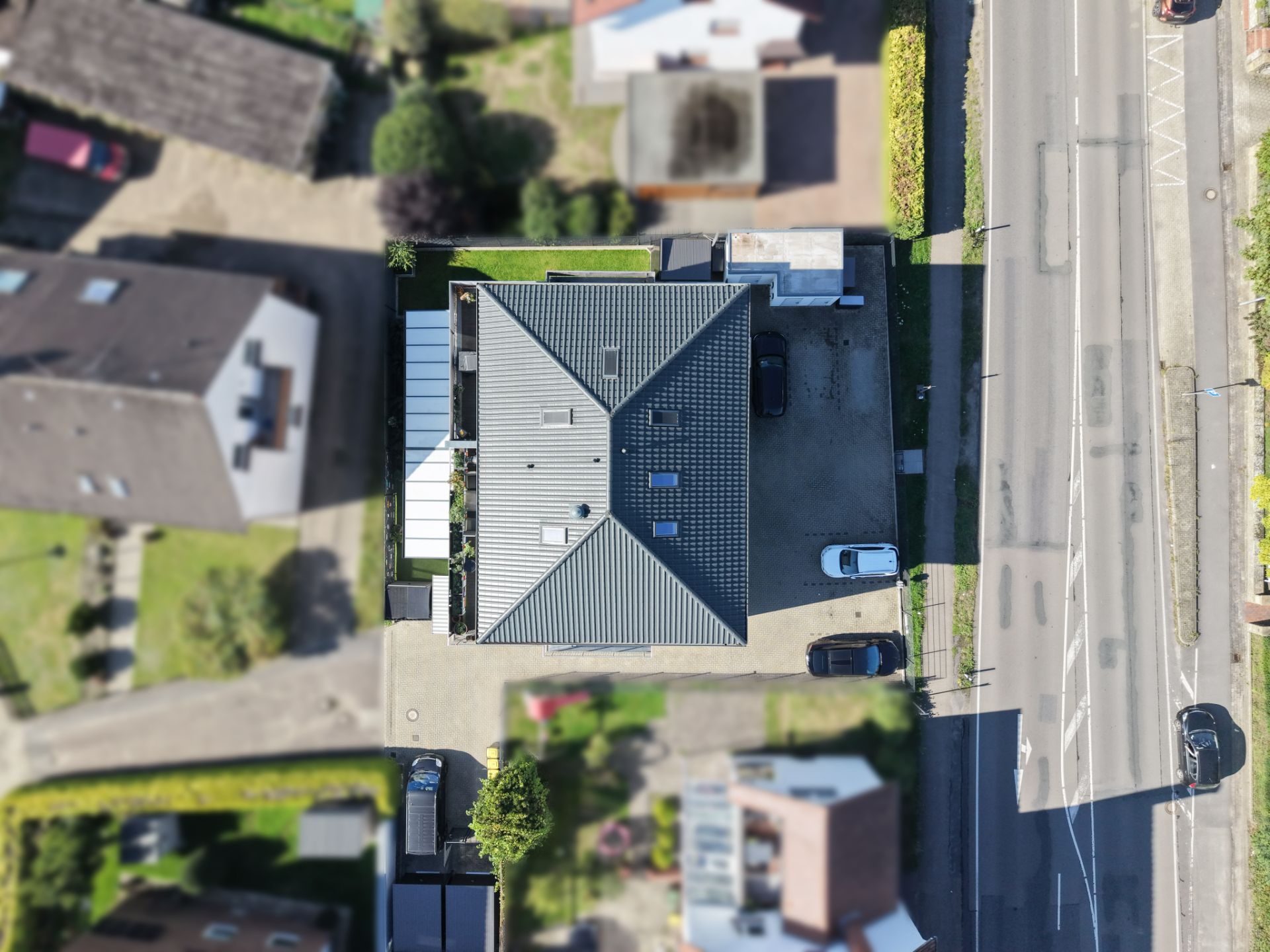 Luftaufnahme eines Hauses mit grauem Dach, umgeben von Straße, Auffahrt und Nachbargebäuden.