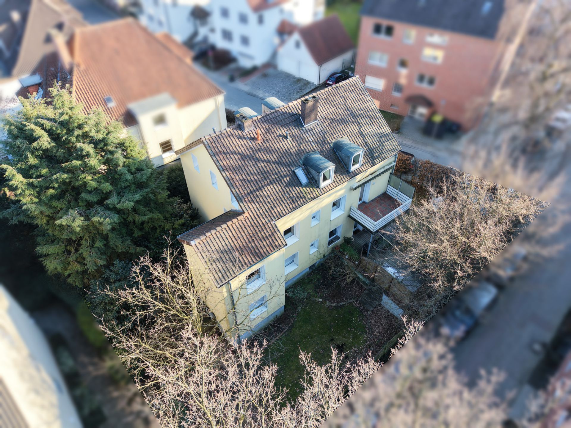 Luftaufnahme eines gelben Wohnhauses mit Garten und Bäumen, umgeben von weiteren Häusern.