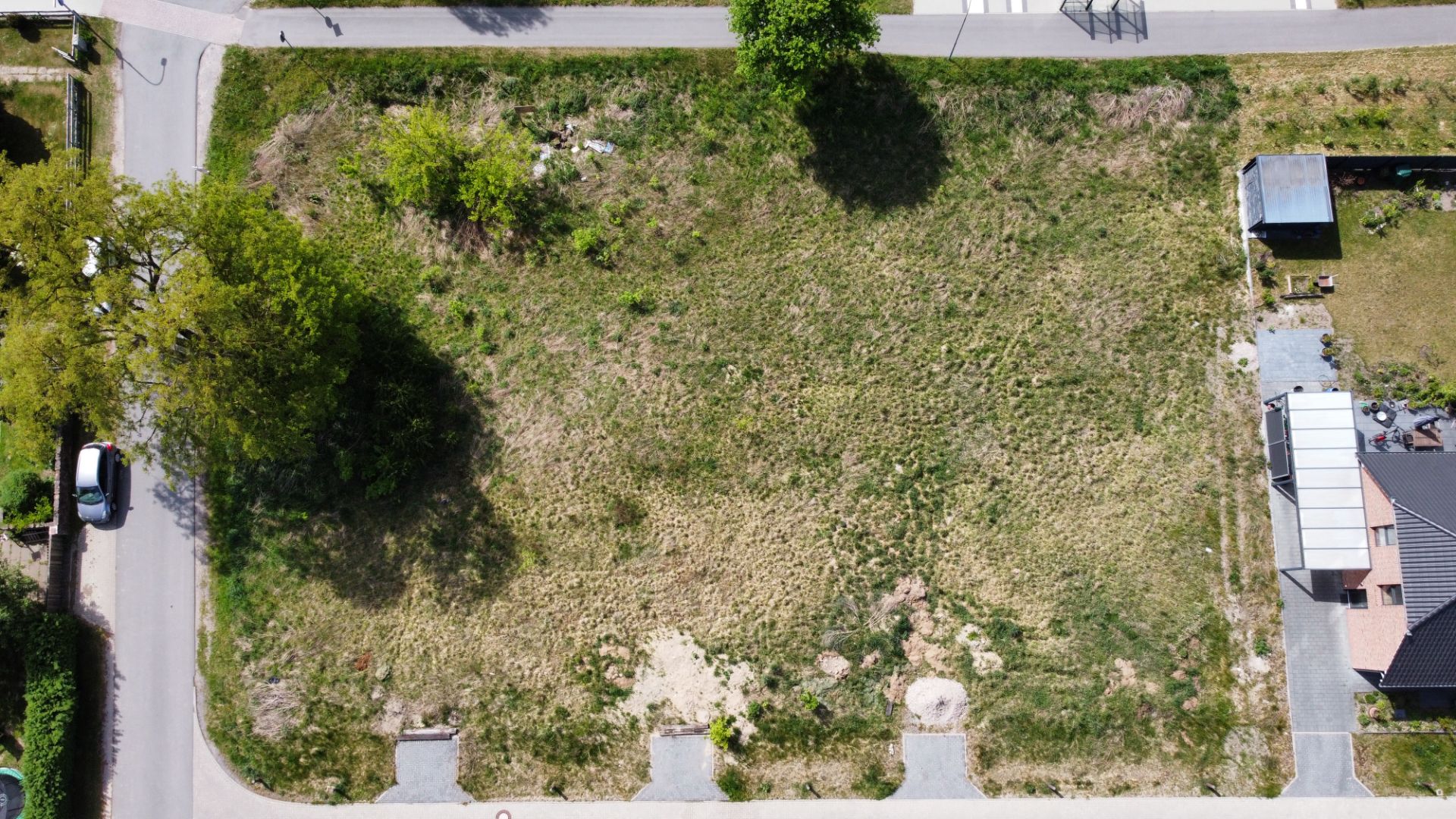 Luftaufnahme eines rechteckigen, unbebauten Grundstücks mit Gras und einzelnen Bäumen an den Rändern.
