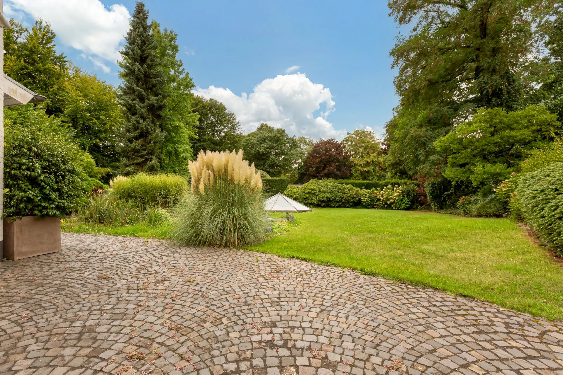 Gepflasterte Terrasse mit Blick auf einen grünen Garten und viele Bäume.