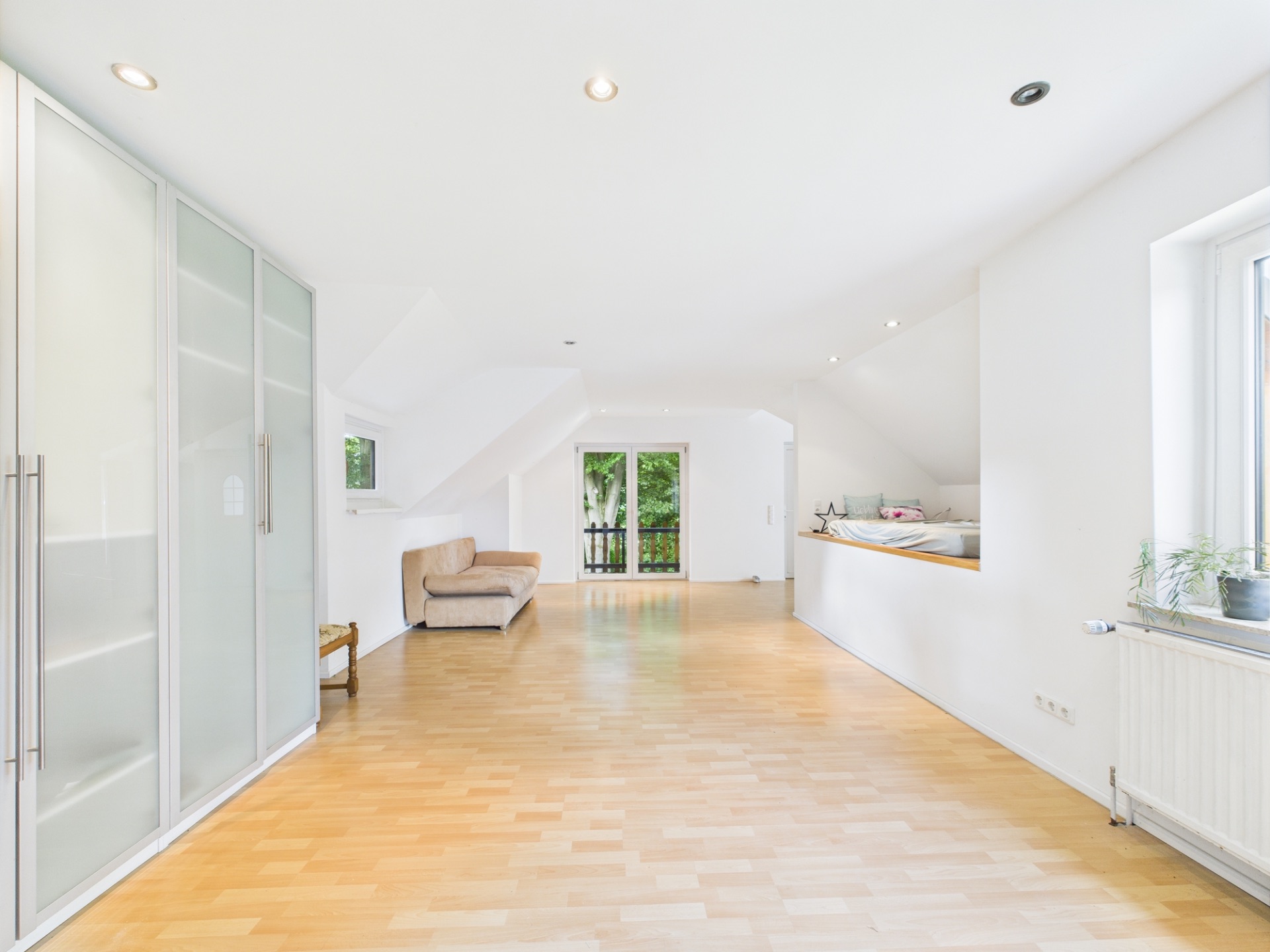 Helles, modernes Wohnzimmer mit Sofa, Einbauschrank, Fenster und Zugang zu einem Balkon.