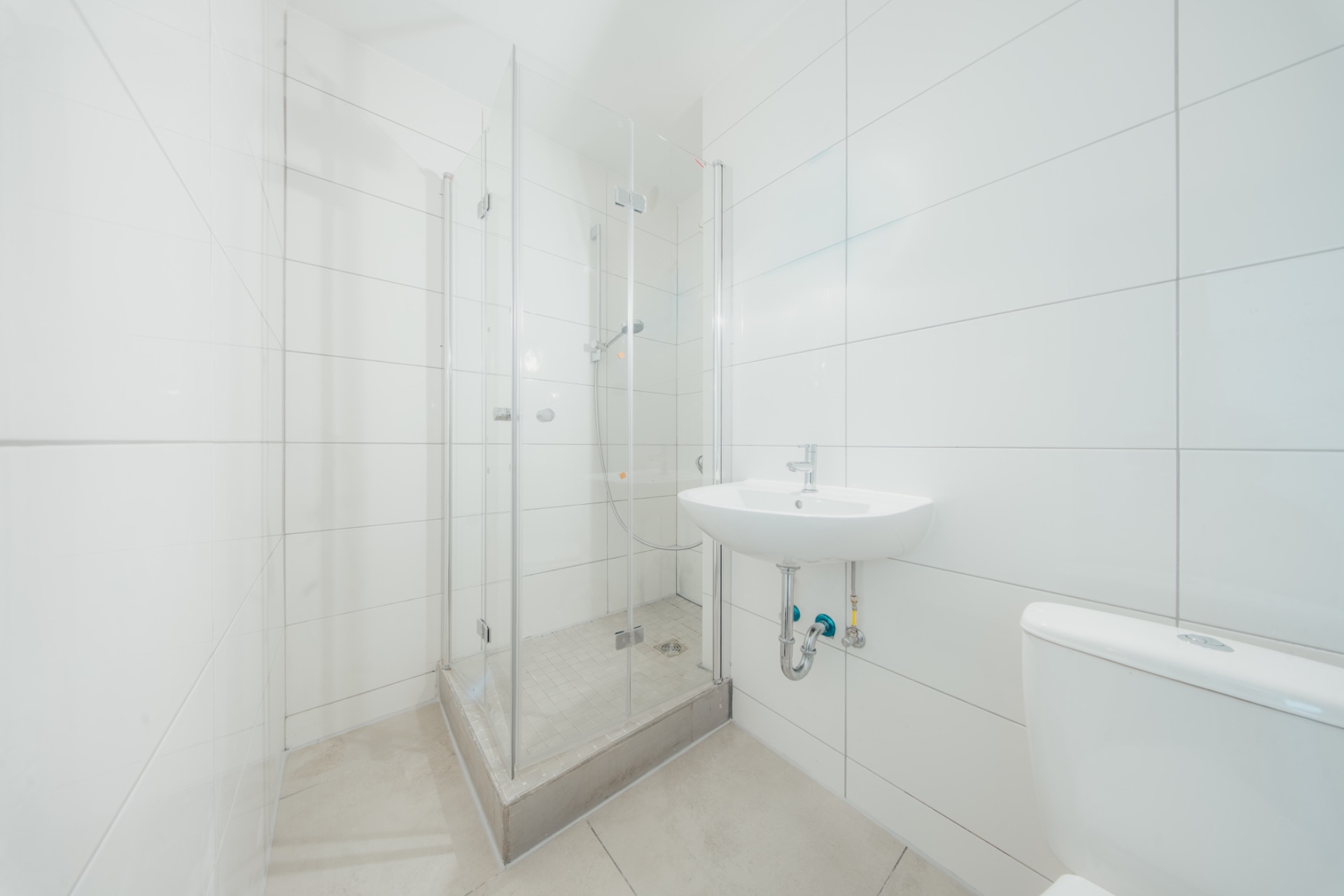 Modernes, weiß gefliestes Bad mit Dusche, Waschbecken und Toilette.