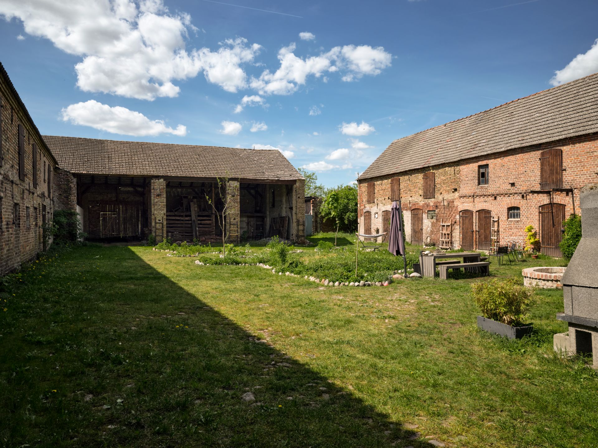 Hof mit Rasenfläche, alten Backsteingebäuden, Gartentisch, Bank und Steinofen.
