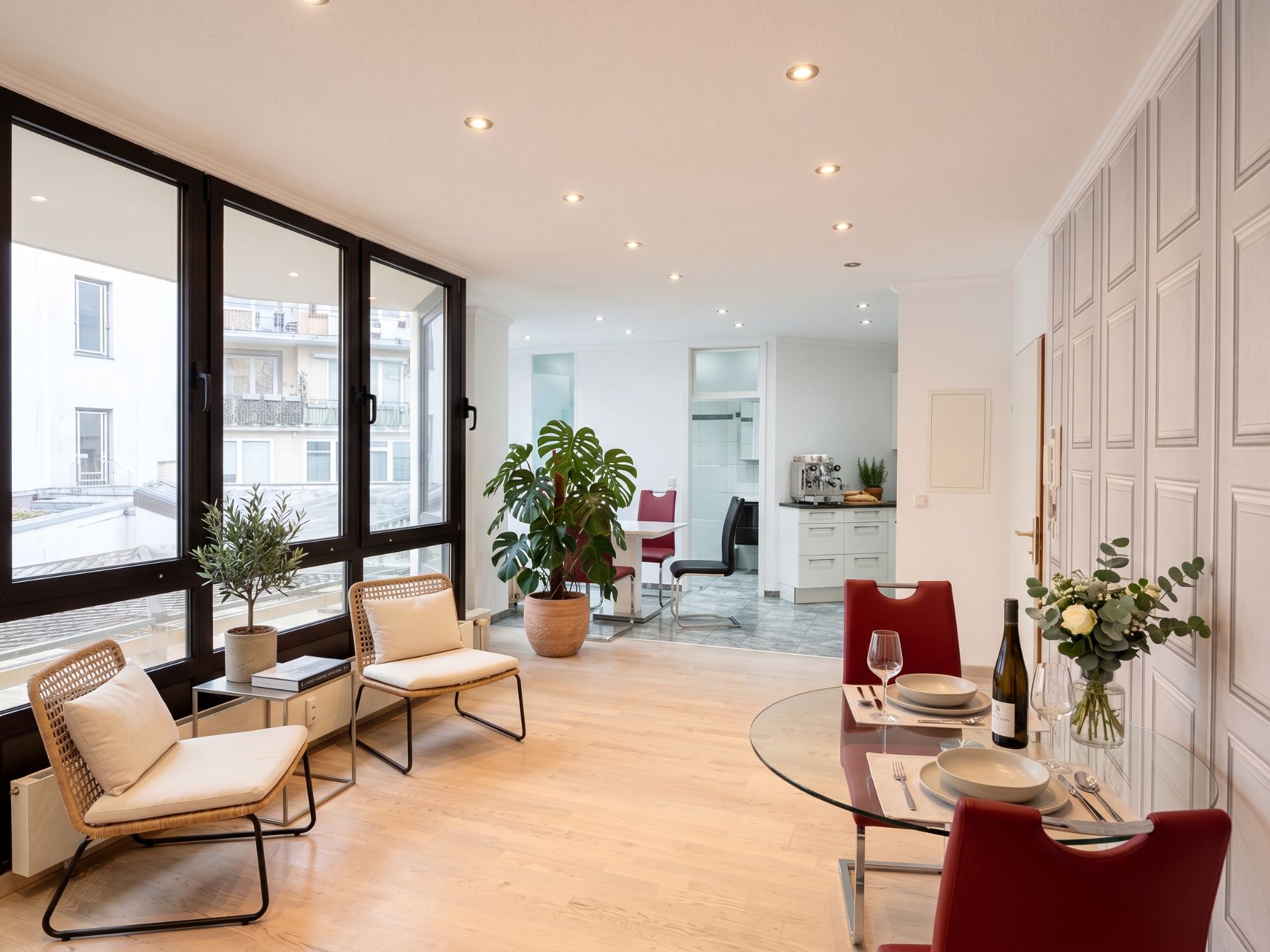 Helles Wohnzimmer mit großen Fenstern, zwei Sesseln, Esstisch und Pflanzen.