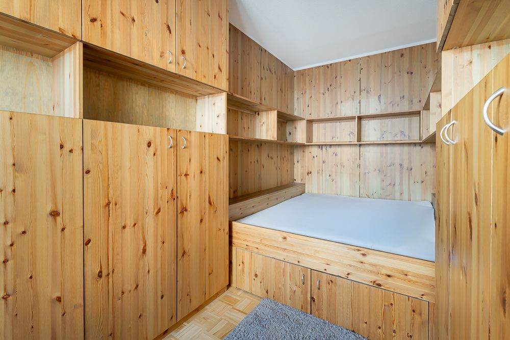 Kleines Schlafzimmer mit Holzmöbeln, Einbauschrank und Bett, grauer Teppich auf Holzfußboden.