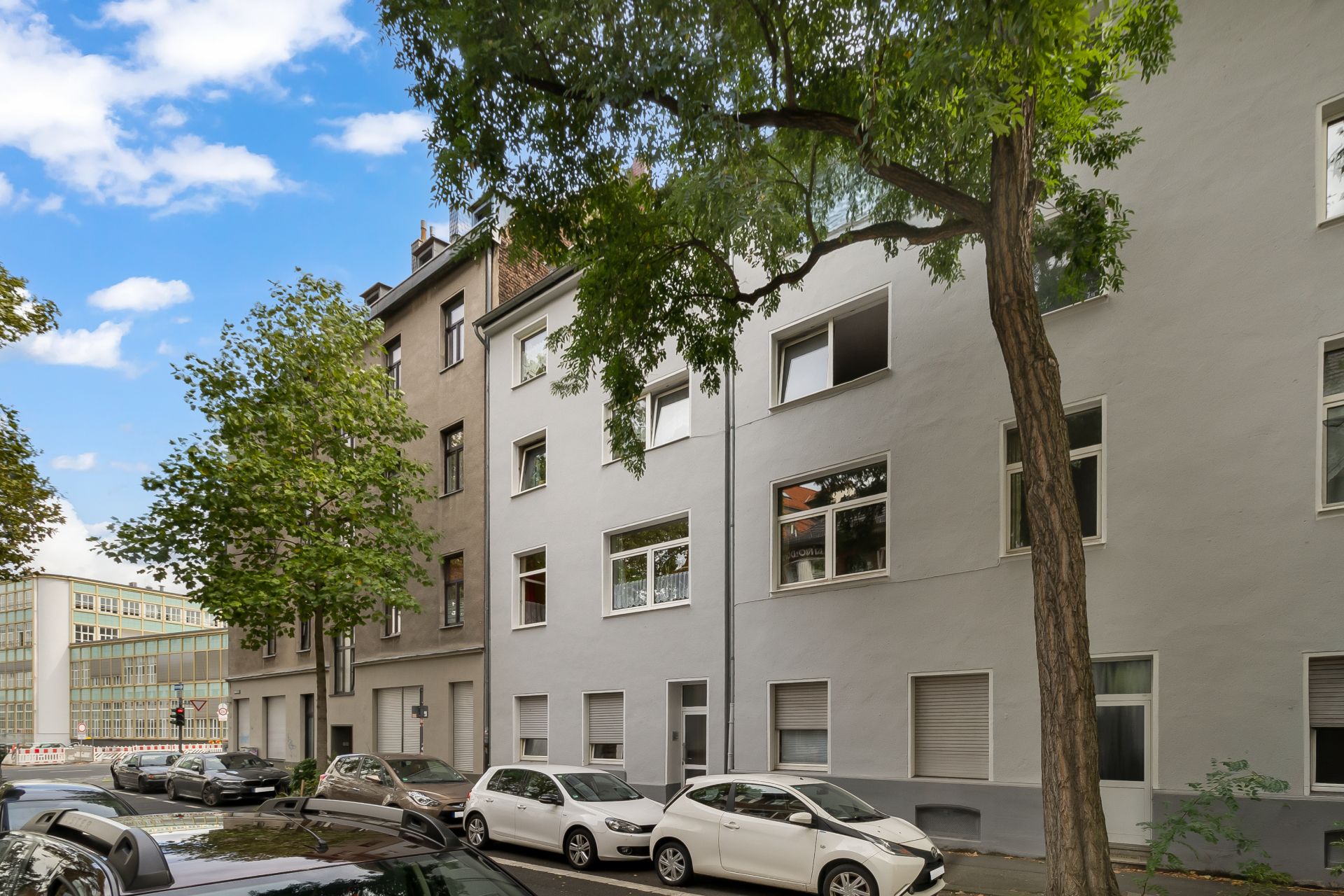 Mehrstöckiges Wohnhaus mit geparkten Autos und Bäumen an der Straße.