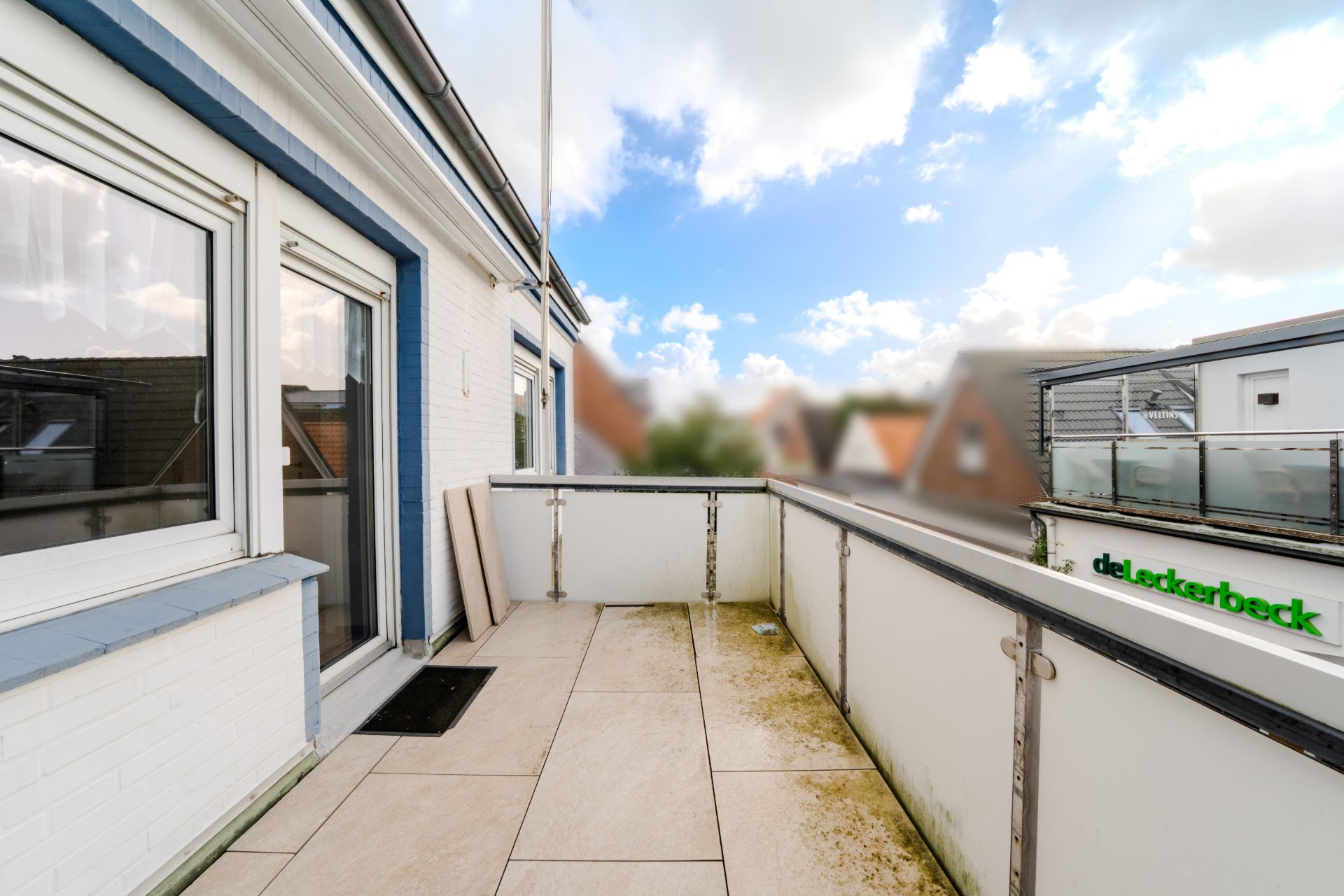 Balkon mit Fliesenboden und Glasgeländer an einem Wohnhaus.