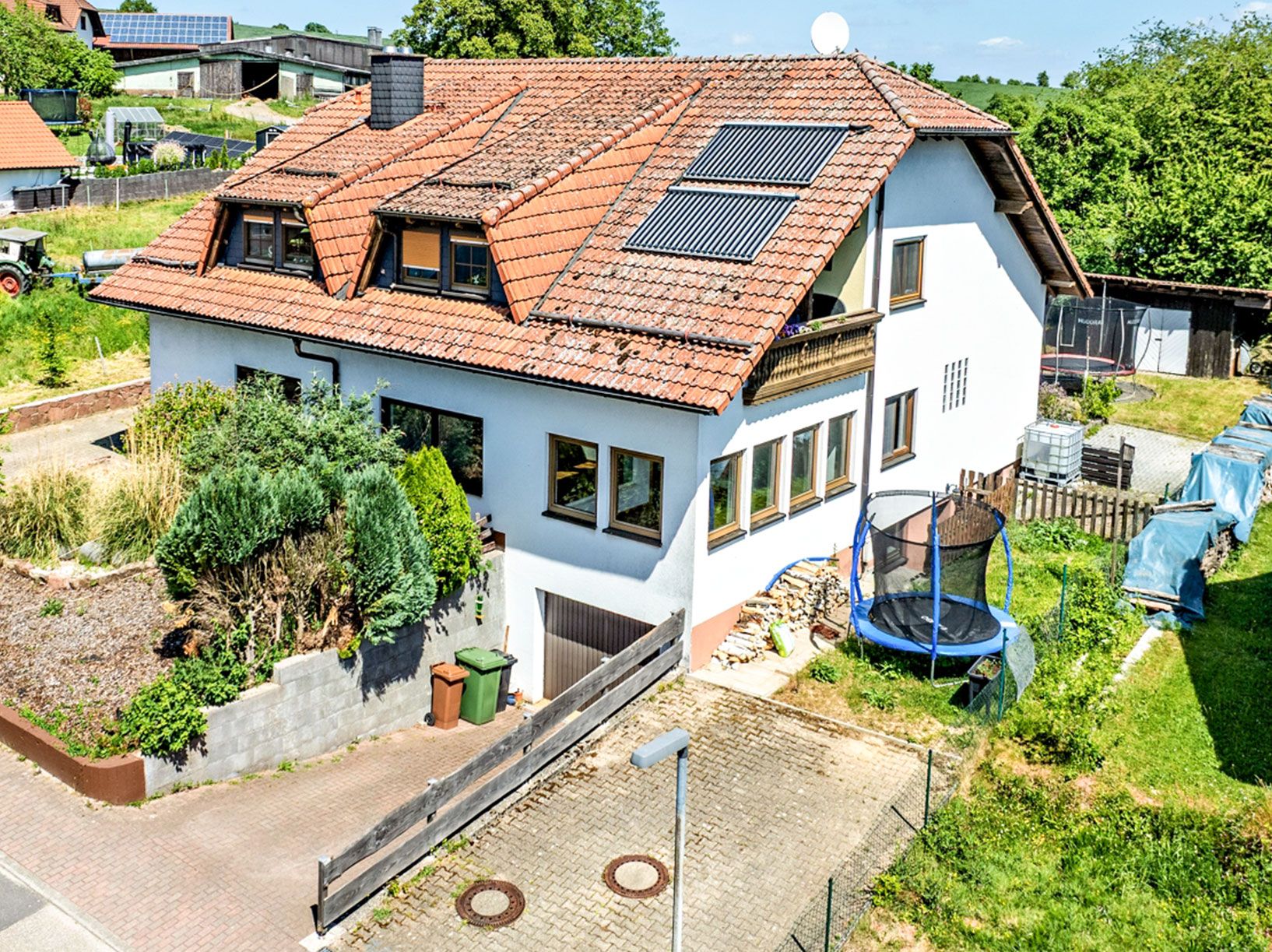 Weißes Wohnhaus mit rotem Dach, Solarpaneelen und einem Trampolin im Garten.