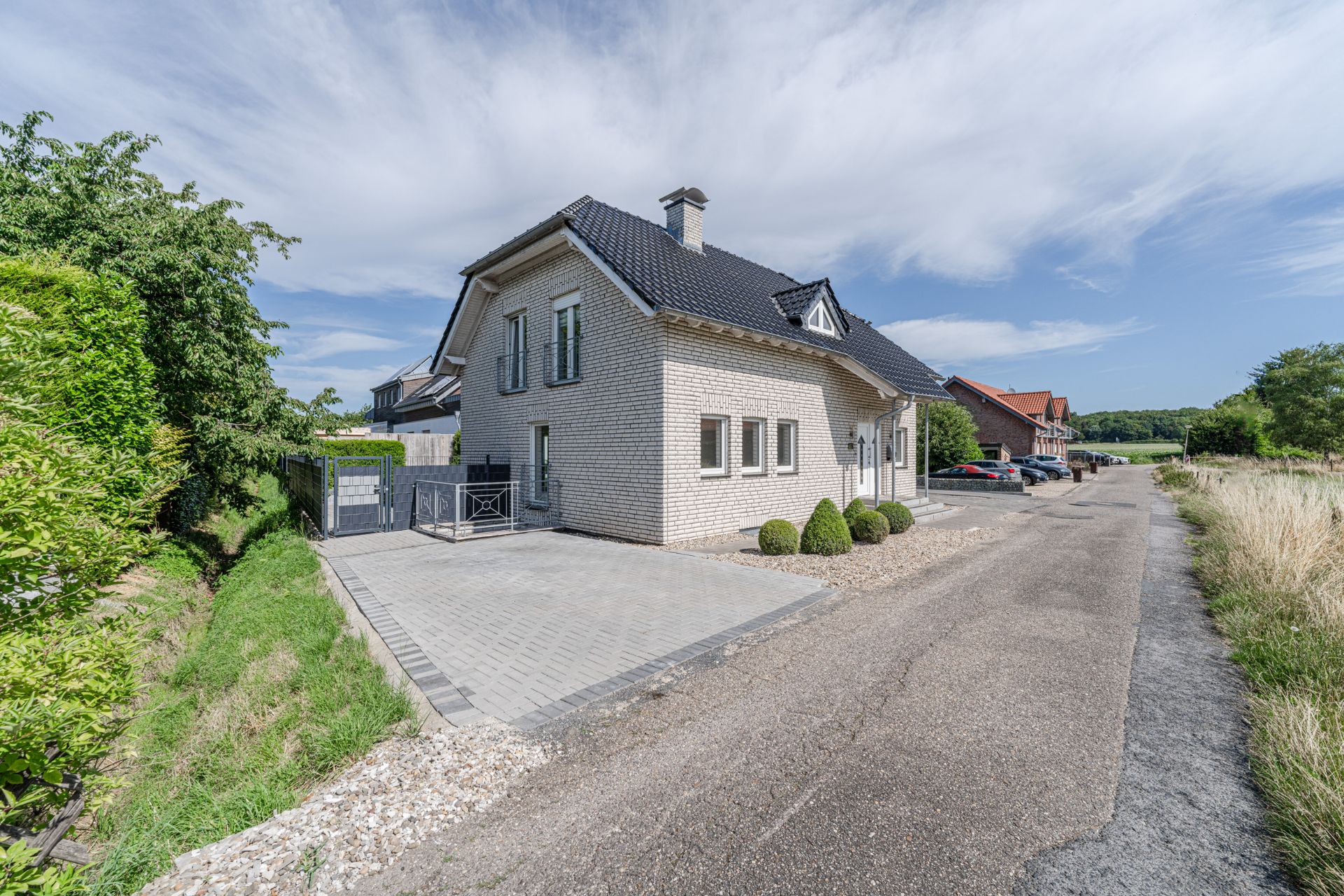 Modernes Einfamilienhaus mit heller Klinkerfassade und schwarzem Dach an einer ruhigen Straße.