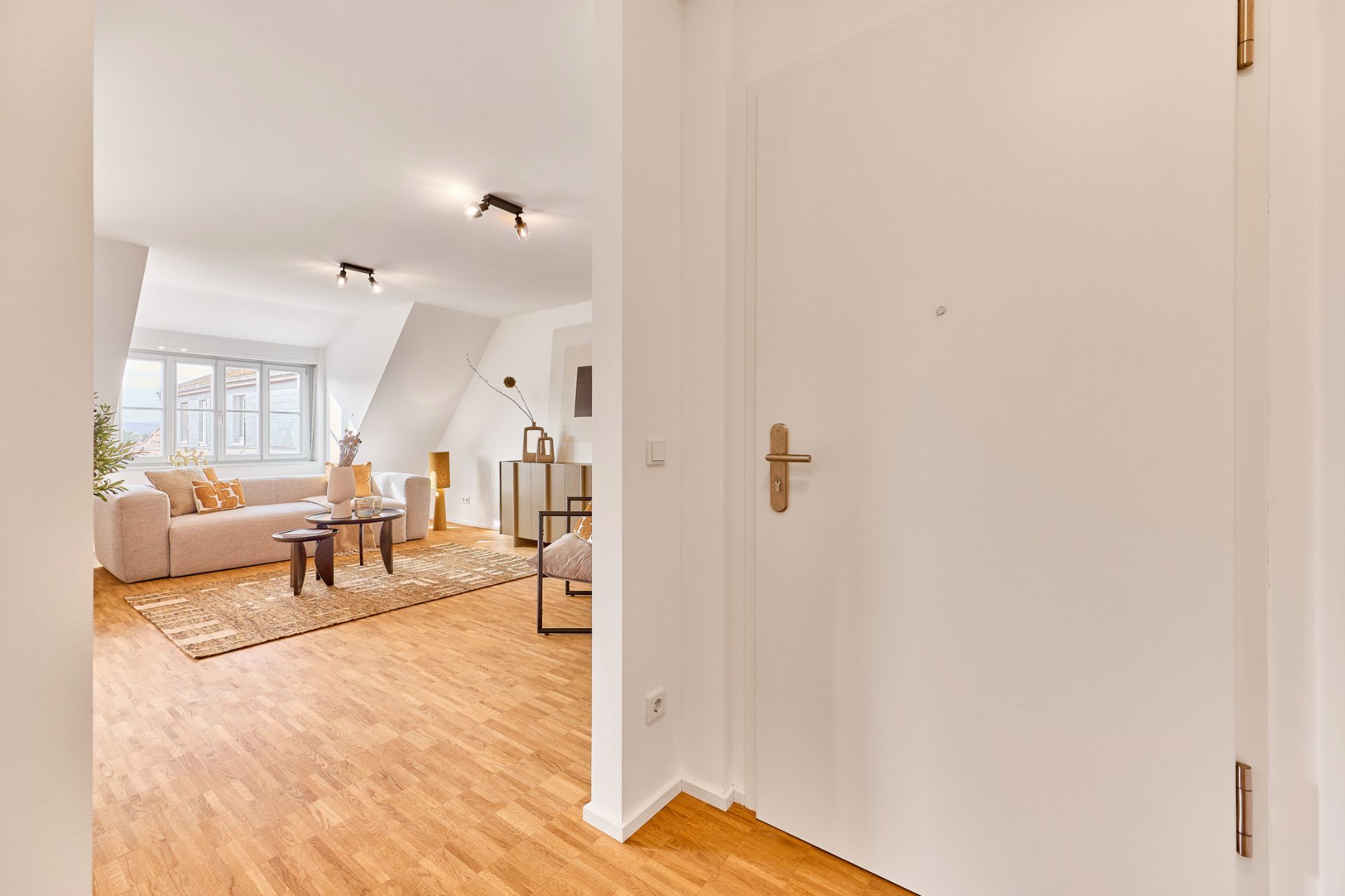 Blick vom Flur in ein helles Wohnzimmer mit Sofa und großen Fenstern.