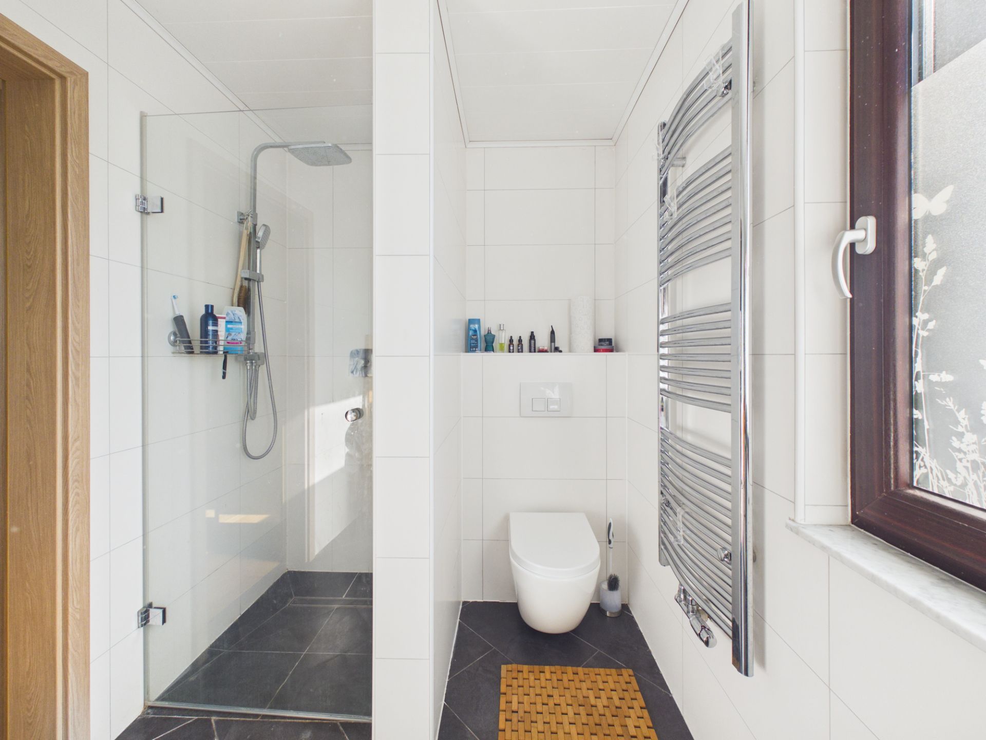 Modernes Badezimmer mit Dusche, Toilette, Handtuchheizung und Fenster.