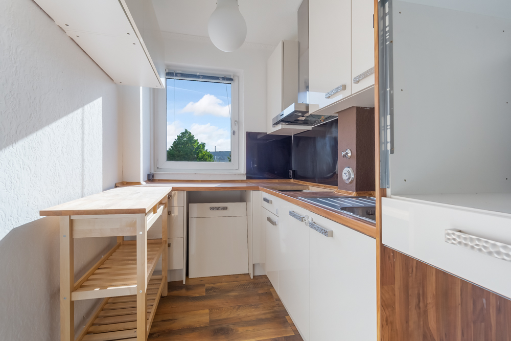 Helle, schmale Küche mit Holzarbeitsplatte, Fenster und weißen Schränken.