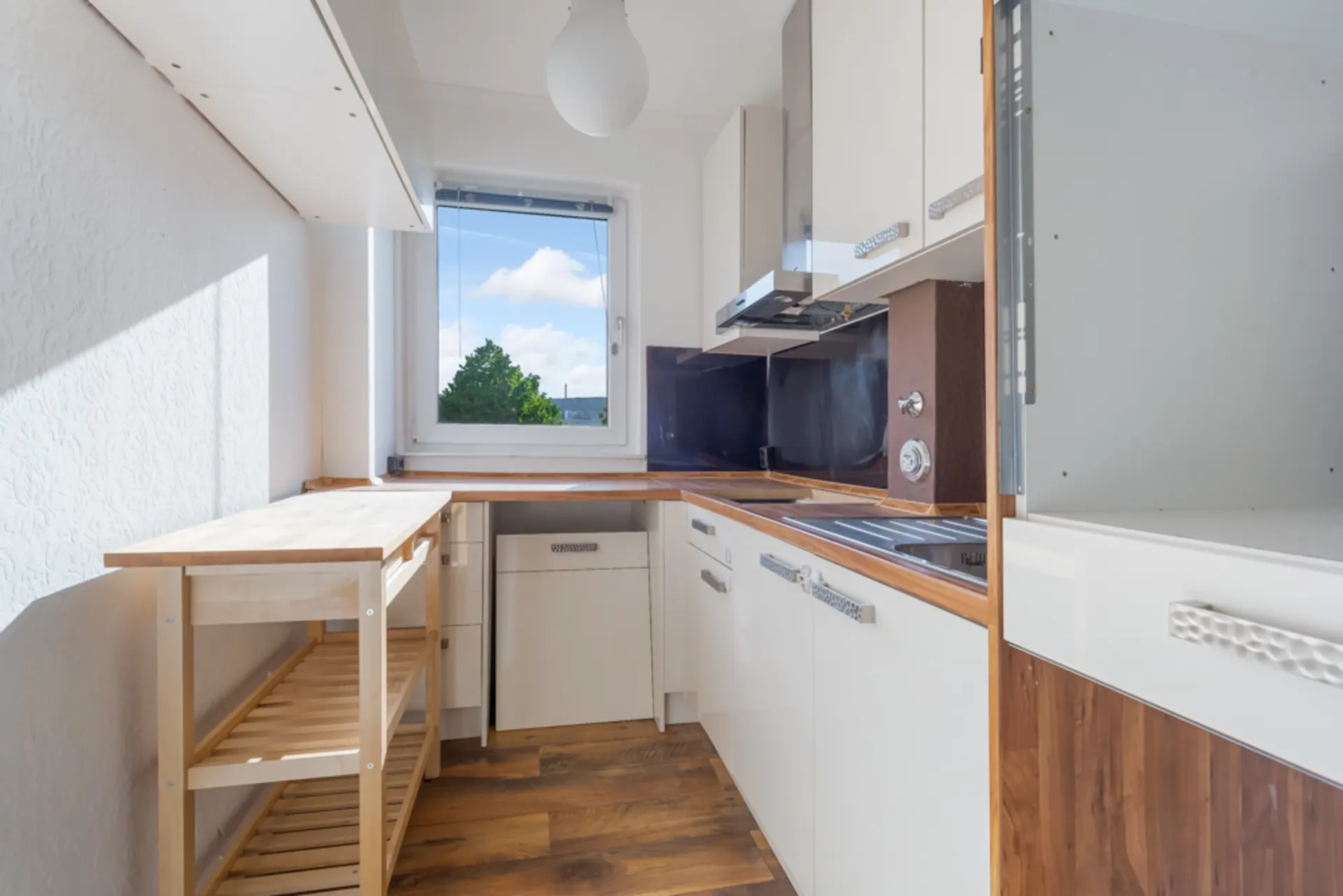 Helle, schmale Küche mit Holzarbeitsplatte, Fenster und weißen Schränken.
