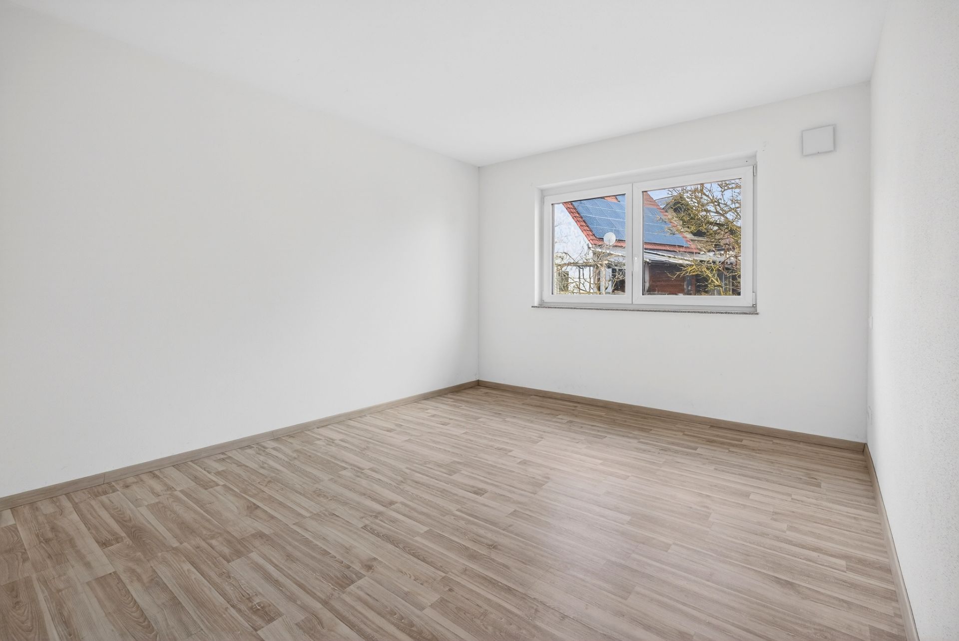 Leerer Raum mit hellem Holzfußboden und großem Fenster, weiße Wände.