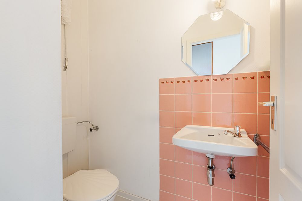 Kleines Badezimmer mit Toilette, Waschbecken, Spiegel und rosa Fliesen an der Wand.