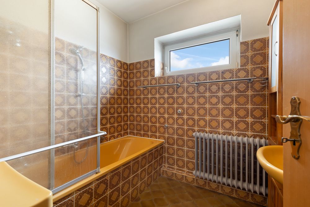 Badezimmer mit gelber Badewanne, gemusterten Fliesen und Fenster.