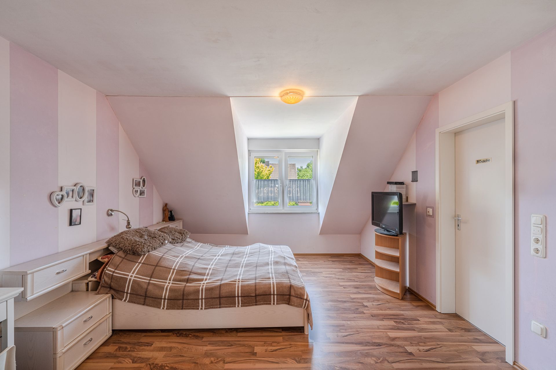 Helles Schlafzimmer mit Doppelbett, Fernseher, Holzfußboden und Fenster mit Blick ins Grüne.