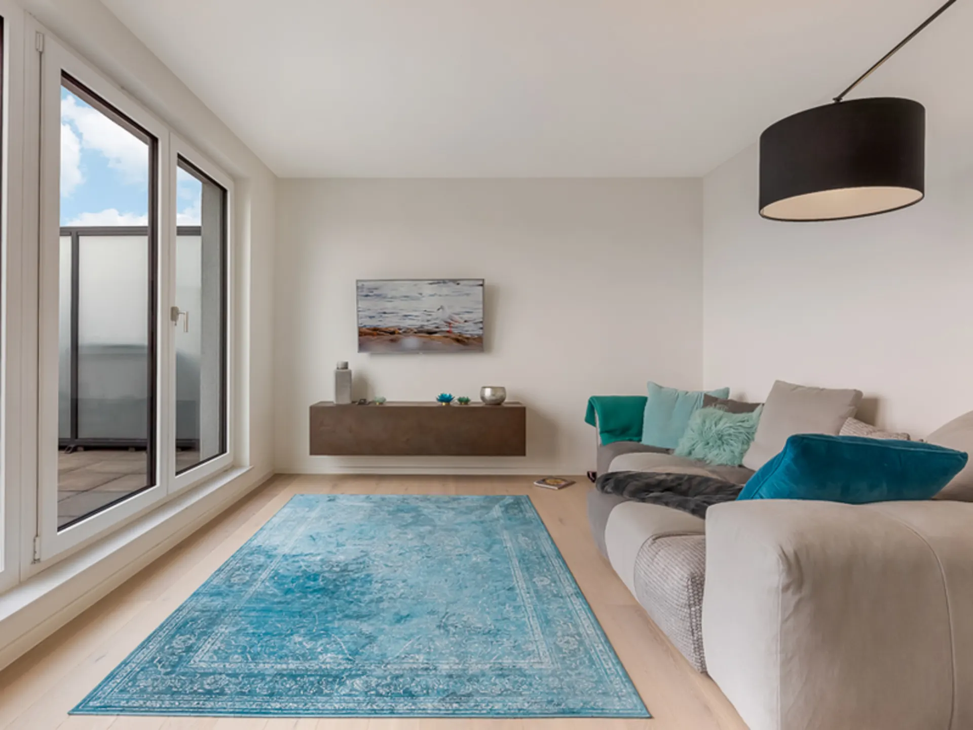 Modernes Wohnzimmer mit großem Fenster, grauem Sofa und blauem Teppich.