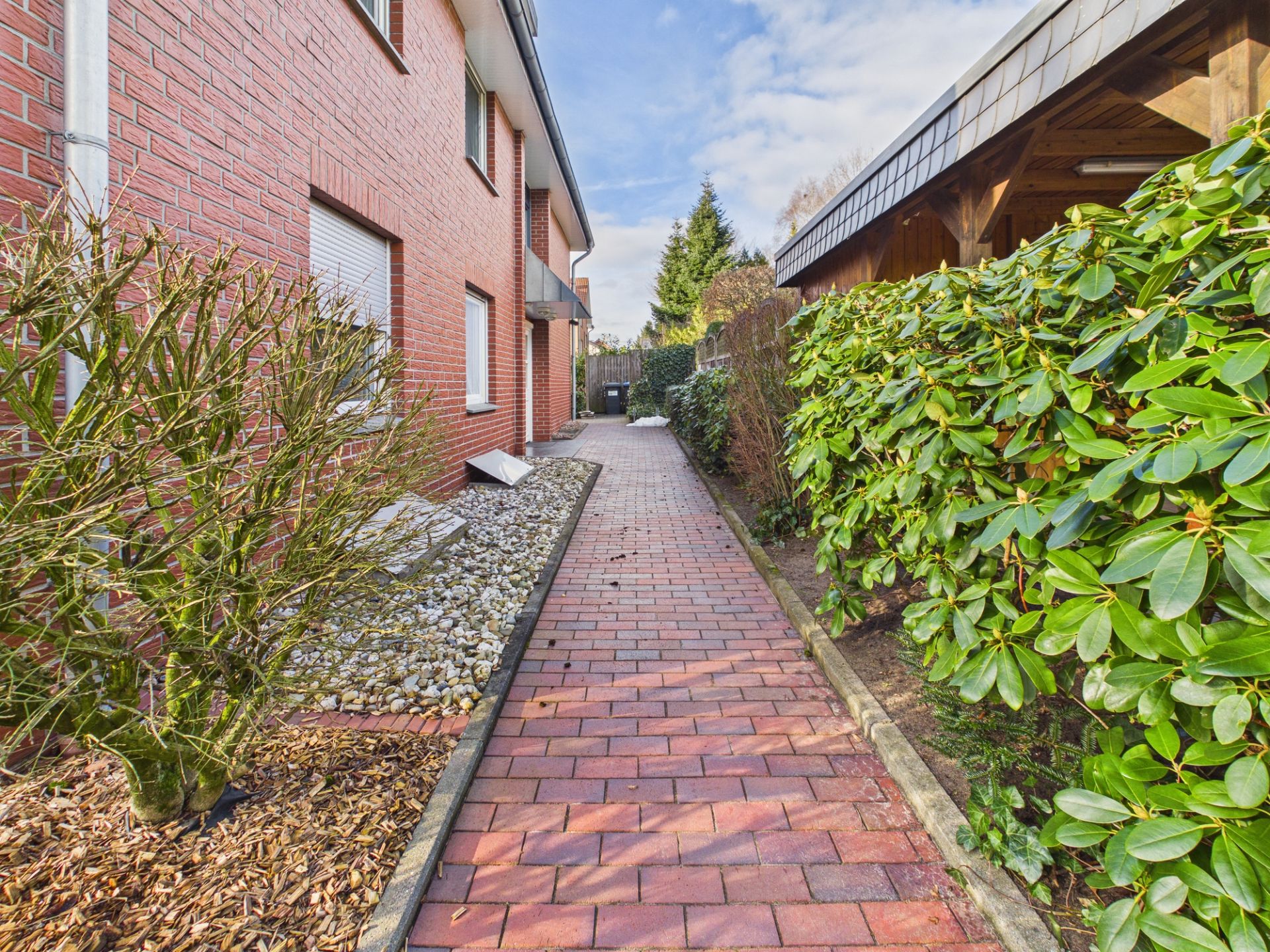Gepflasterter Weg neben einem Wohnhaus mit Hecken und Steinbeet.
