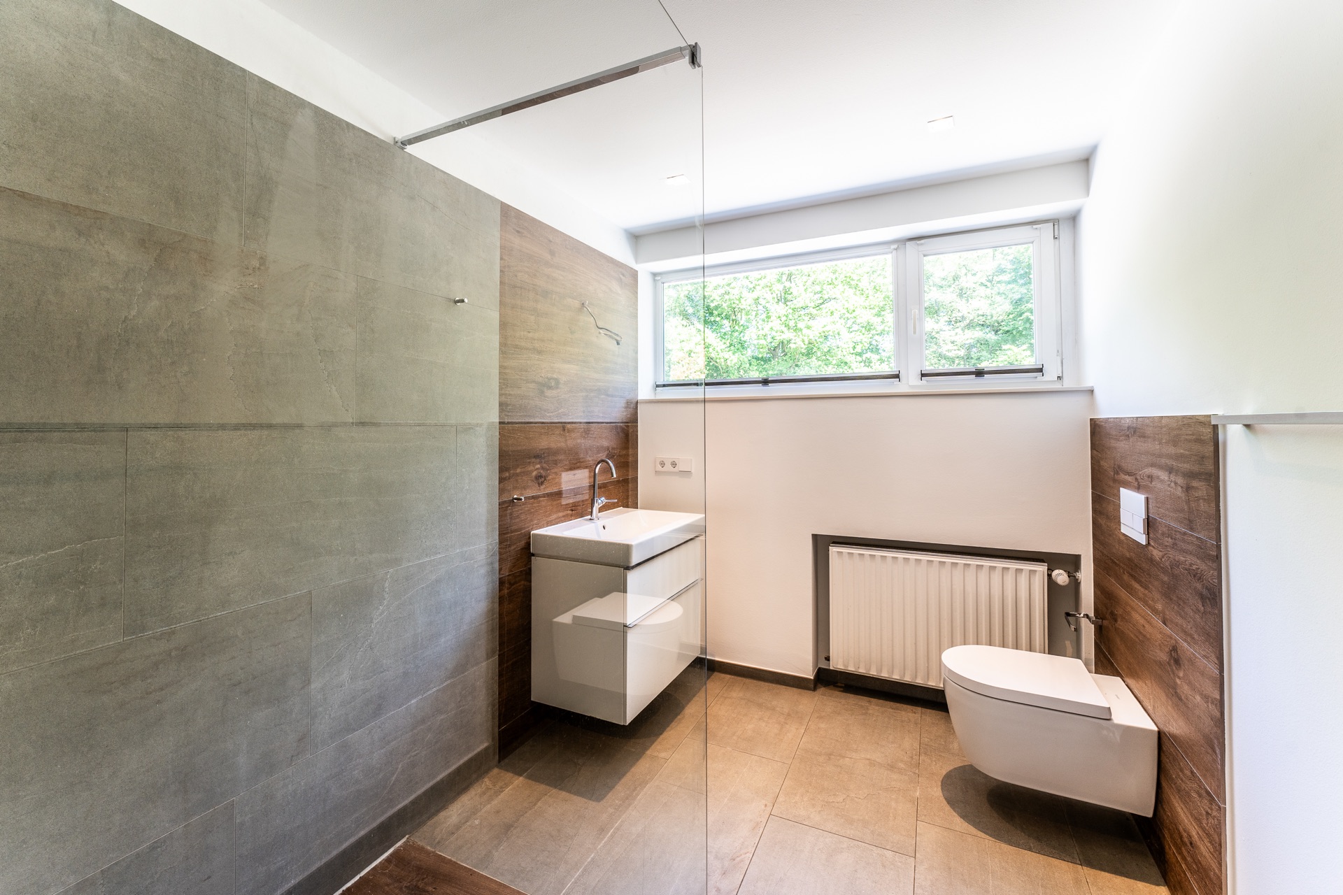 Modernes Badezimmer mit Hänge-WC, Waschbecken, großem Fenster und Fliesenboden.