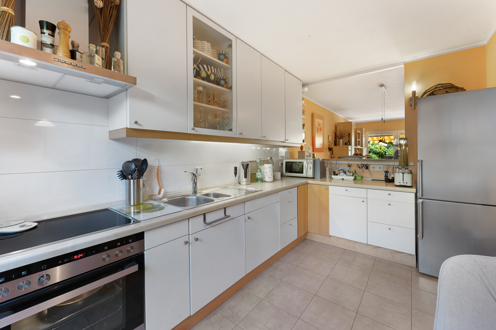 Moderne Küche mit weißen Schränken, Herd, Spüle, Kühlschrank und Küchenutensilien.