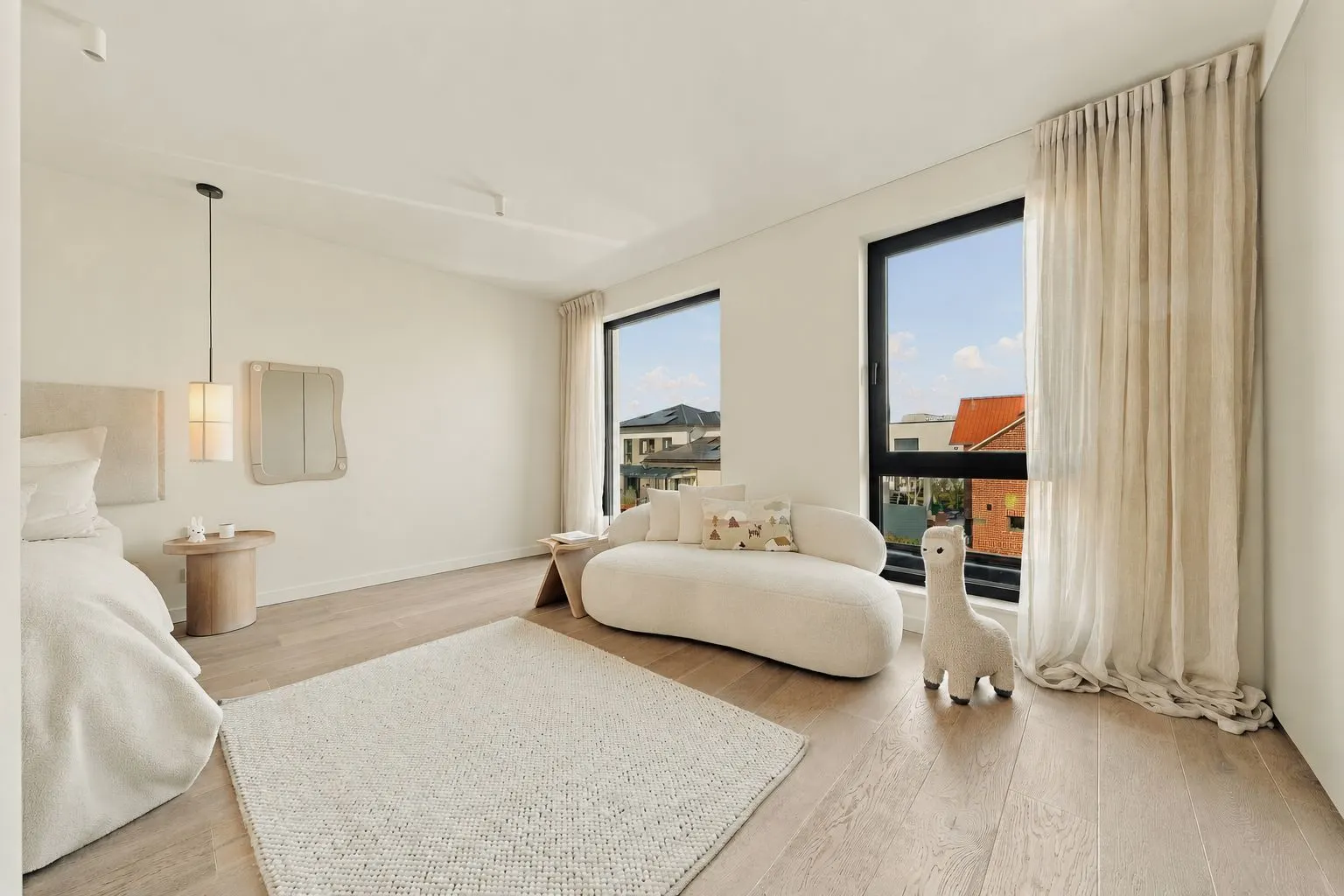 Helles Schlafzimmer mit Bett, Sofa, Teppich, großem Fenster und Plüsch-Lama auf Holzfußboden.