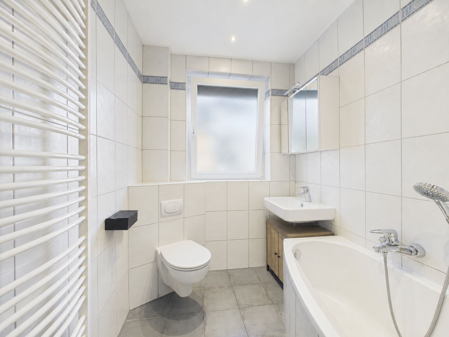 Helles Badezimmer mit Badewanne, WC, Waschbecken, Spiegel und Fenster.