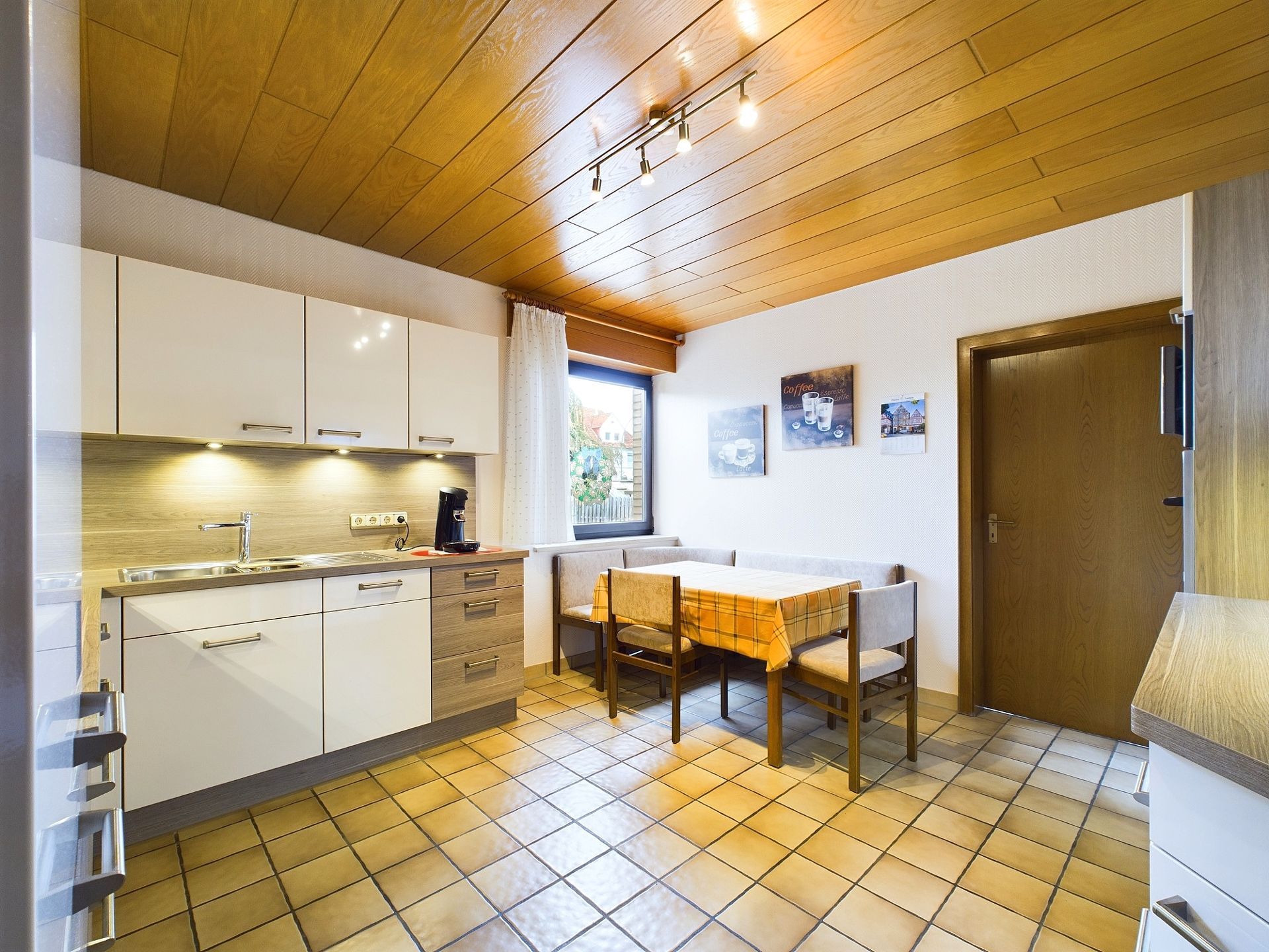 Helle Küche mit Essbereich, Holzboden und -decke, L-förmiger Sitzbank und Fenster.