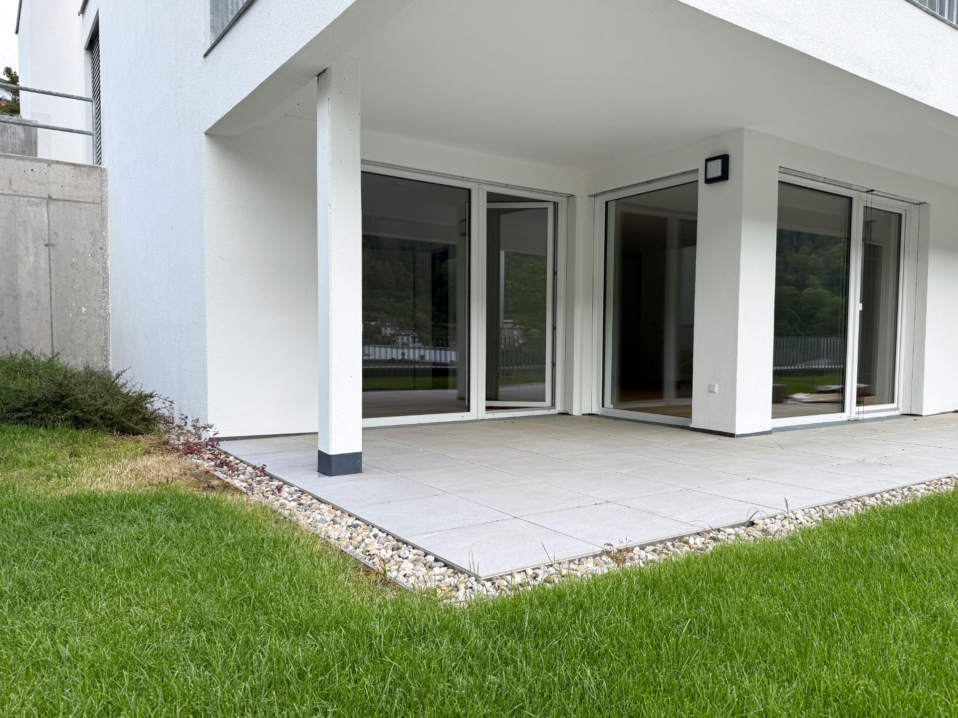 Überdachte Terrasse mit großen Glas-Schiebetüren und angrenzender Rasenfläche.