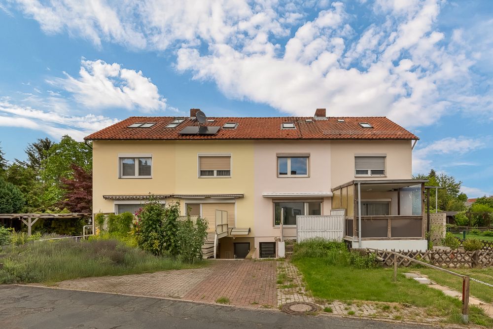 Zweistöckiges Wohnhaus mit rotem Dach und Garten, Auffahrt führt zu einer Garage im Untergeschoss.